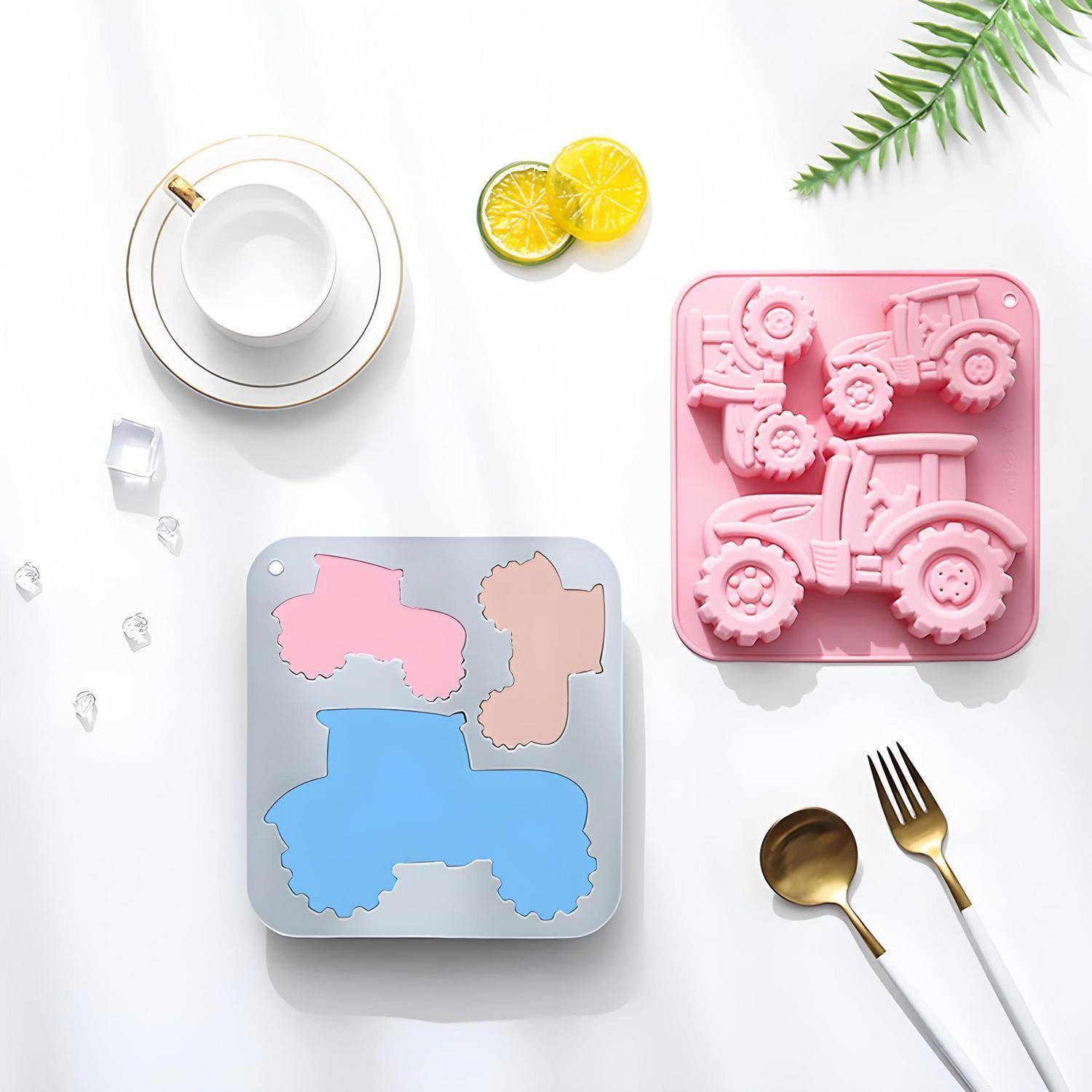 Draufsicht eines Stillebens mit rosa und blauen traktorförmigen Gussformen, einer Teetasse, Zitronenscheiben, Gabel und Löffel auf weißem Hintergrund.