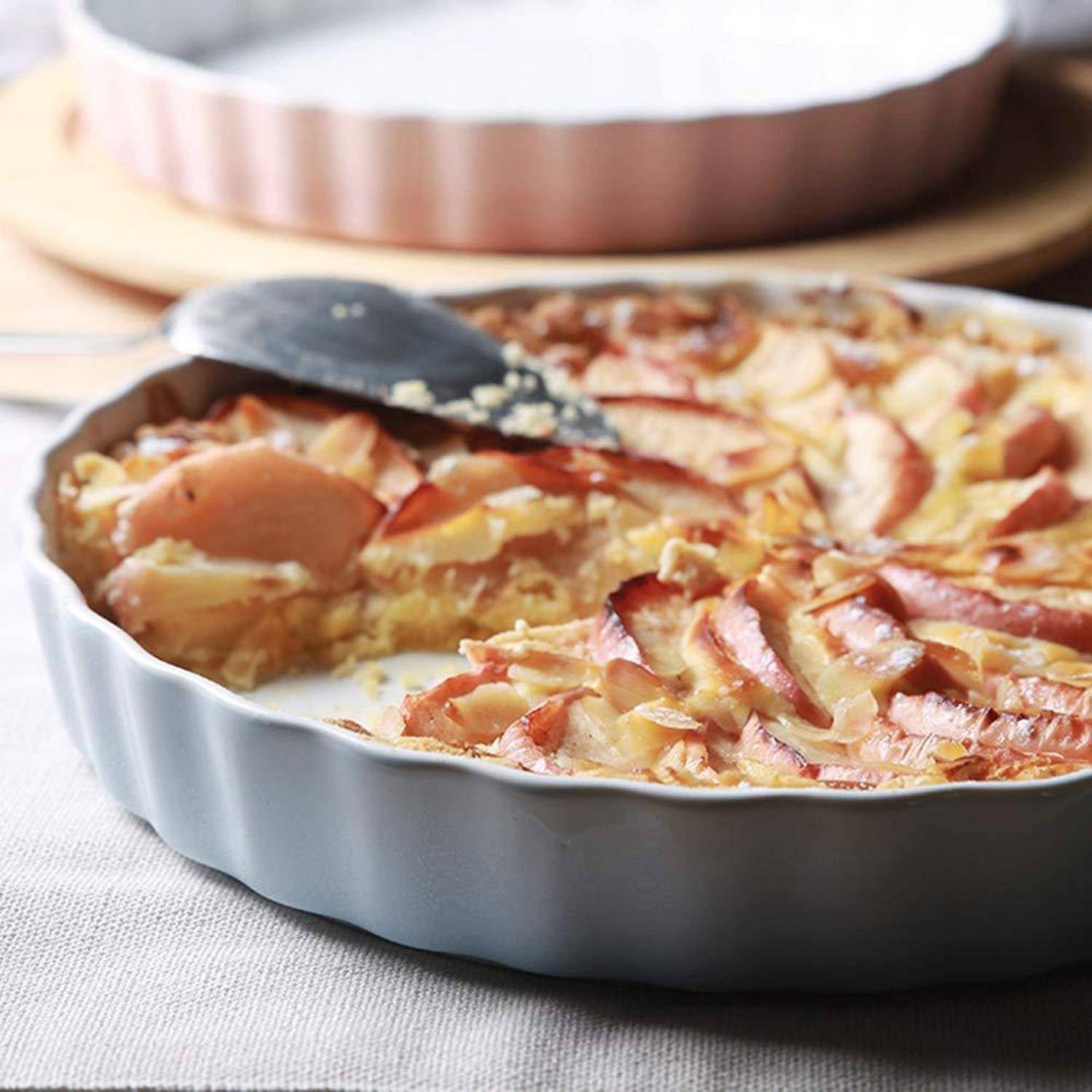 Gebackener Apfelkuchen in einer runden Keramikschüssel, wobei eine Tortenheber ein Stück hebt.