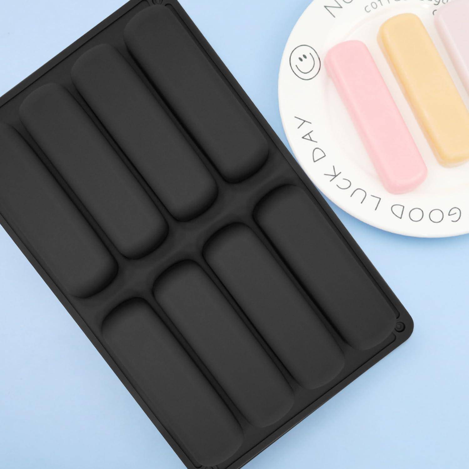 Schwarze rechteckige Eis-Lolly-Form mit sechs langen Vertiefungen neben einem runden Teller mit drei Pastellfarben-Eis-Lollys auf hellblauem Hintergrund.