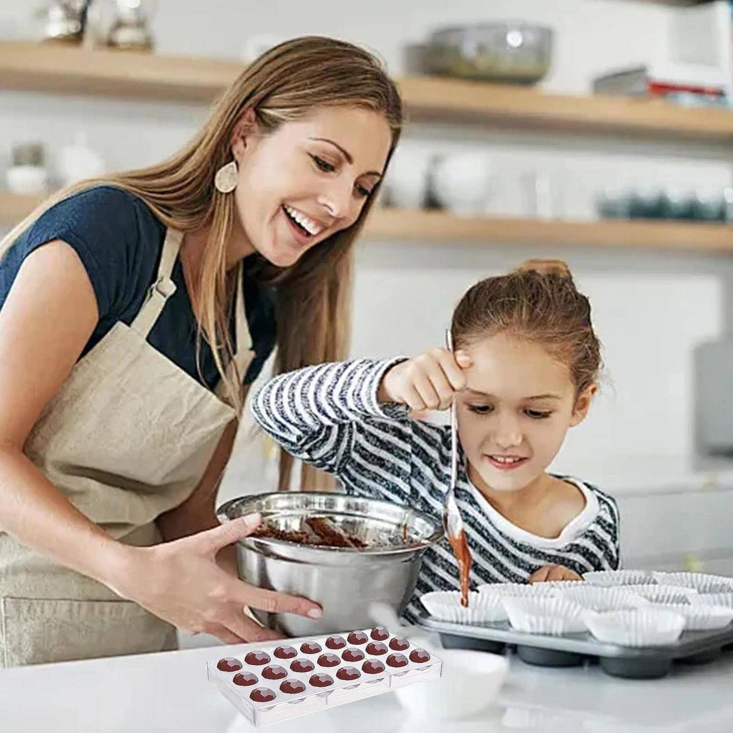Frau und junges Mädchen backen zusammen in einer Küche, löffeln Teig in Muffinförmchen, mit einem Tablett mit Schokoladenchips auf der Arbeitsplatte.