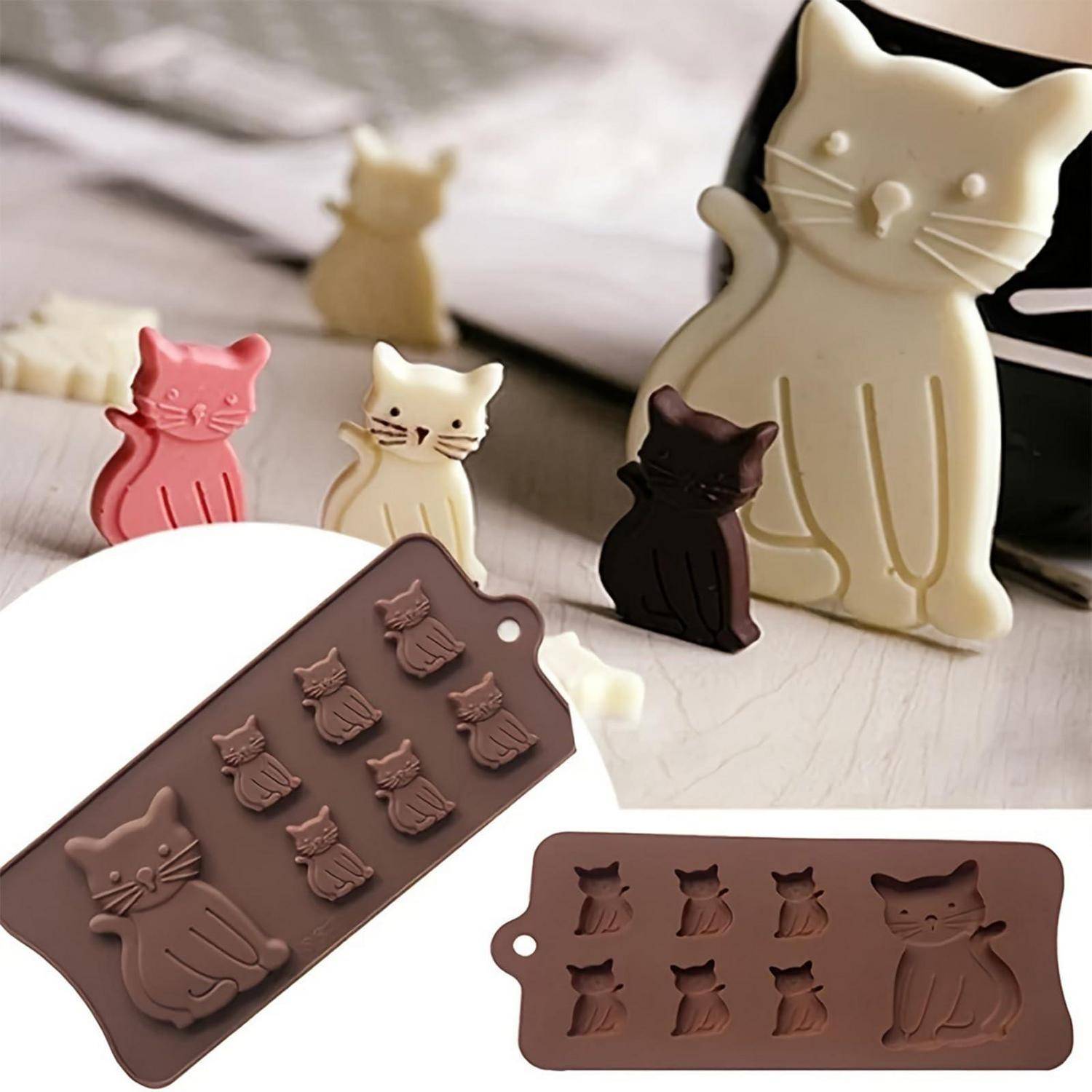 Katzenförmige Silikonformen und fertige Pralinen in Rosa, Creme, Dunkelbraun und Weiß, zusammen auf einer hellen Oberfläche angeordnet.