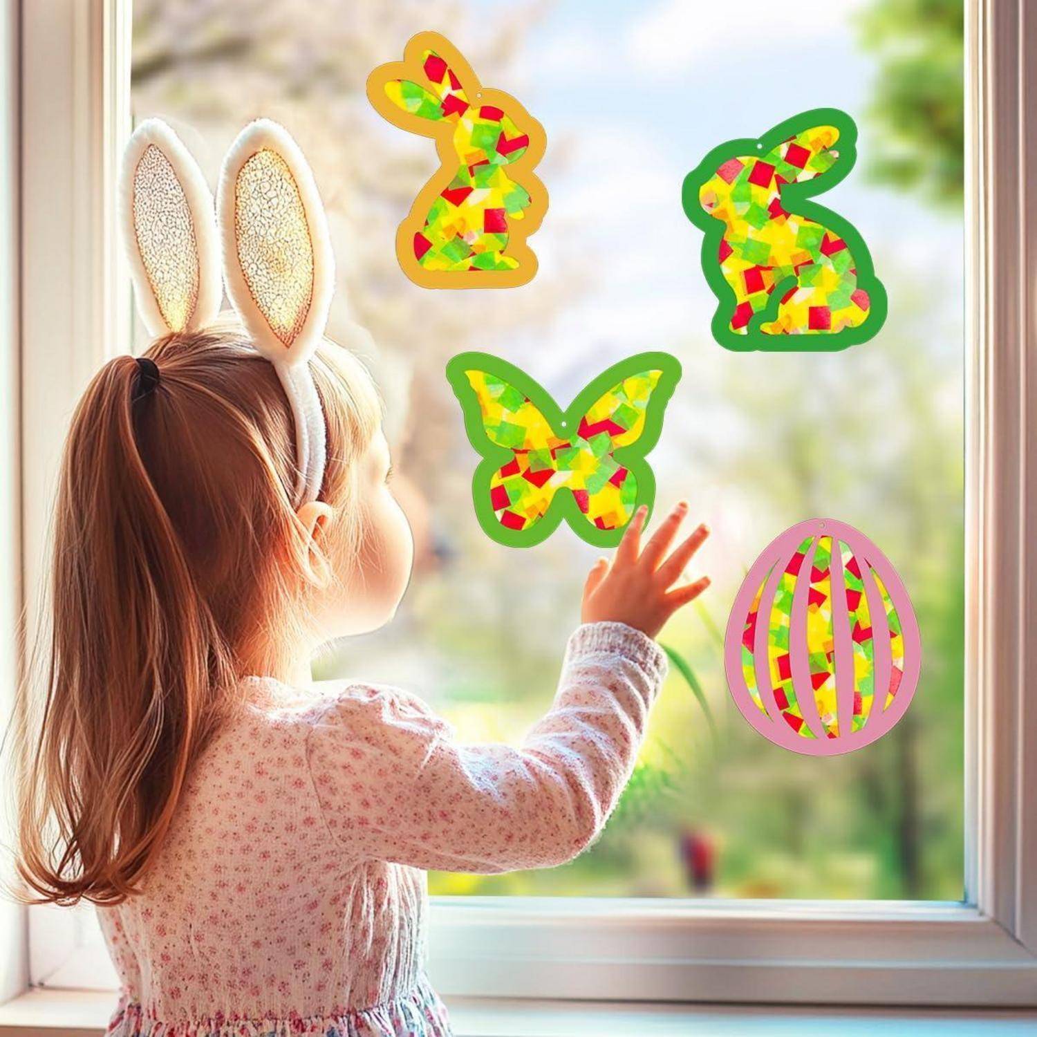 Junges Mädchen mit Hasenohren greift nach bunten Osterdekoration an einem Fenster.