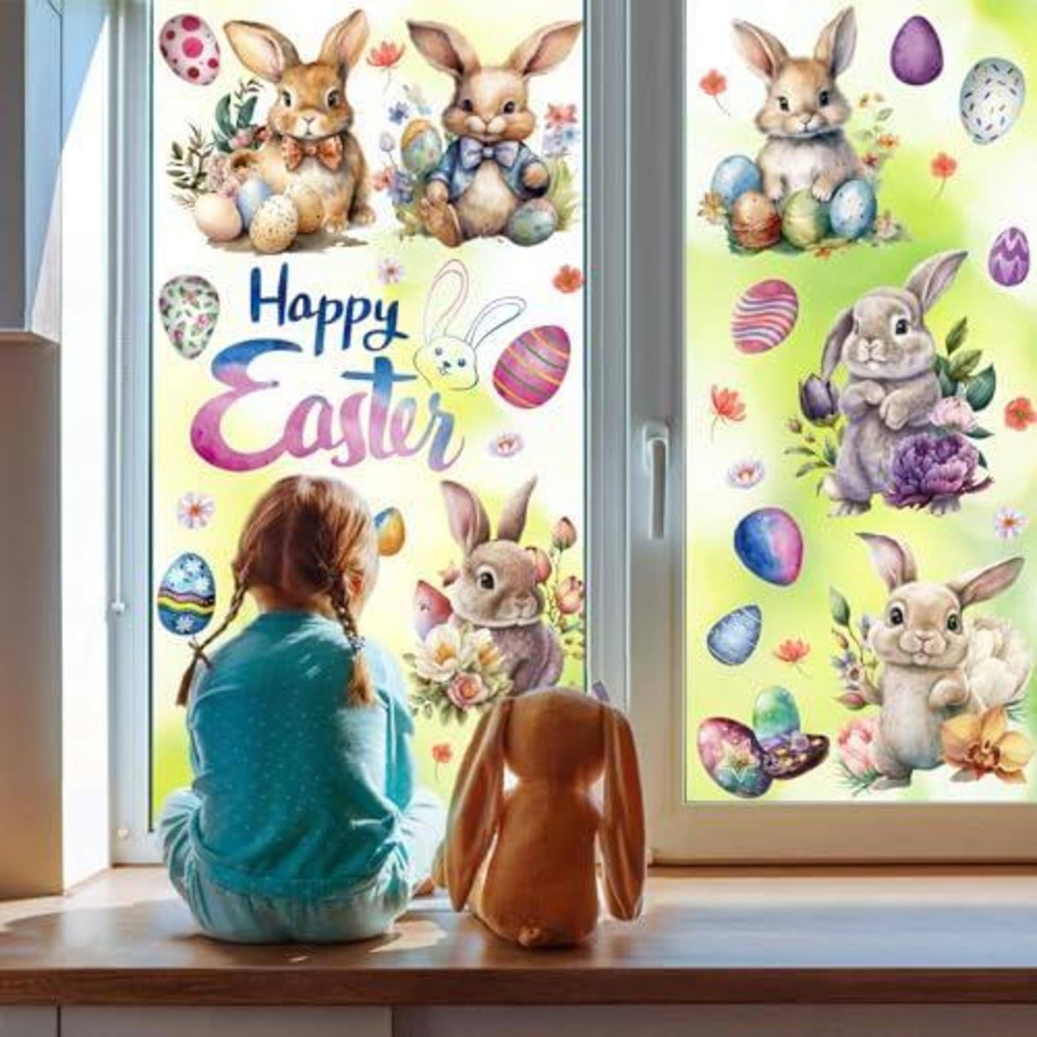Ein Kind sitzt auf einer Fensterbank neben einem Hund und schaut sich leuchtende Oster-Fensteraufkleber mit Hasen, Eiern und dem Text „Frohe Ostern" an.