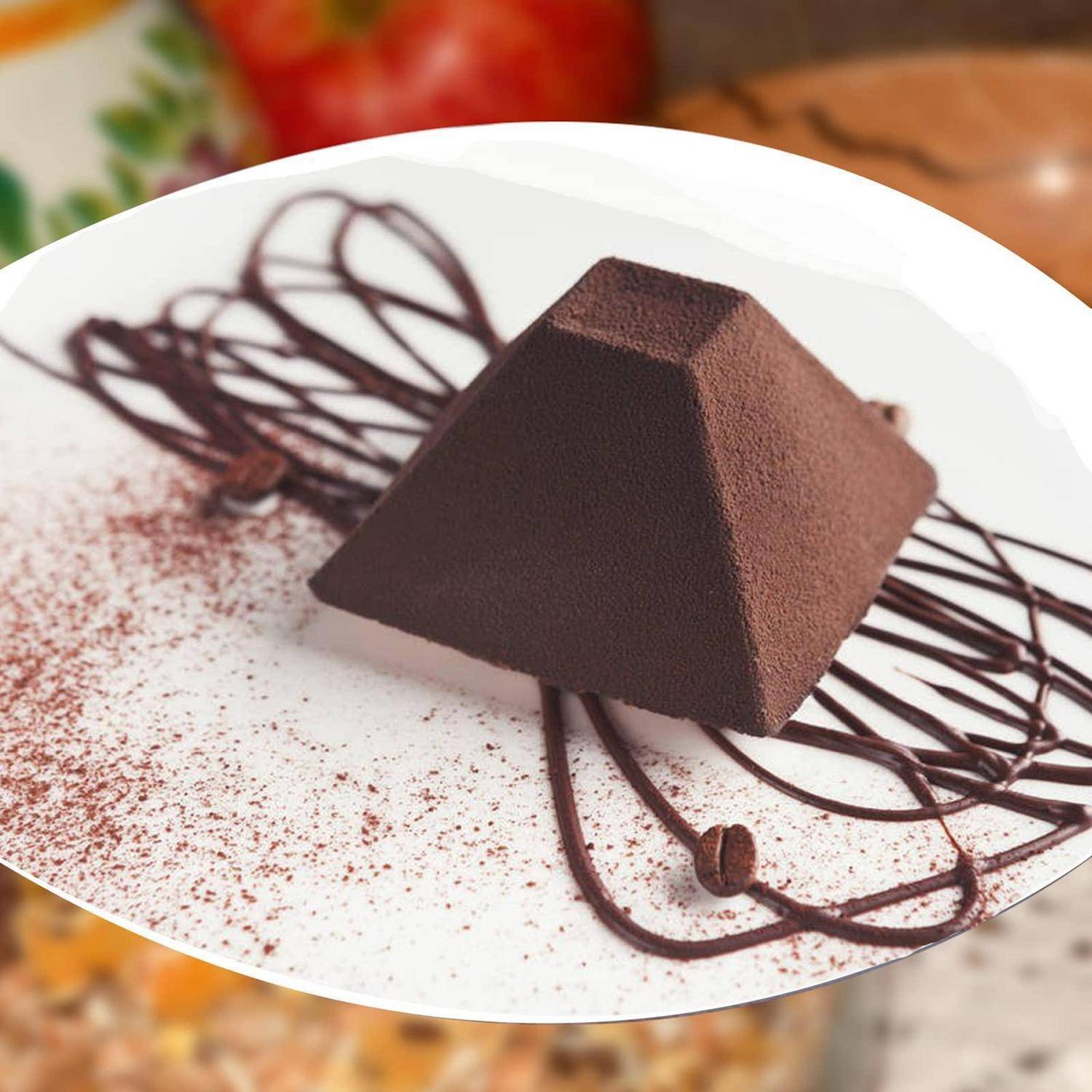 Ein Schokoladenmousse-Dessert in Pyramidenform auf einem weißen Teller, beträufelt mit Schokoladensauce und mit Kakaopulver bestäubt.