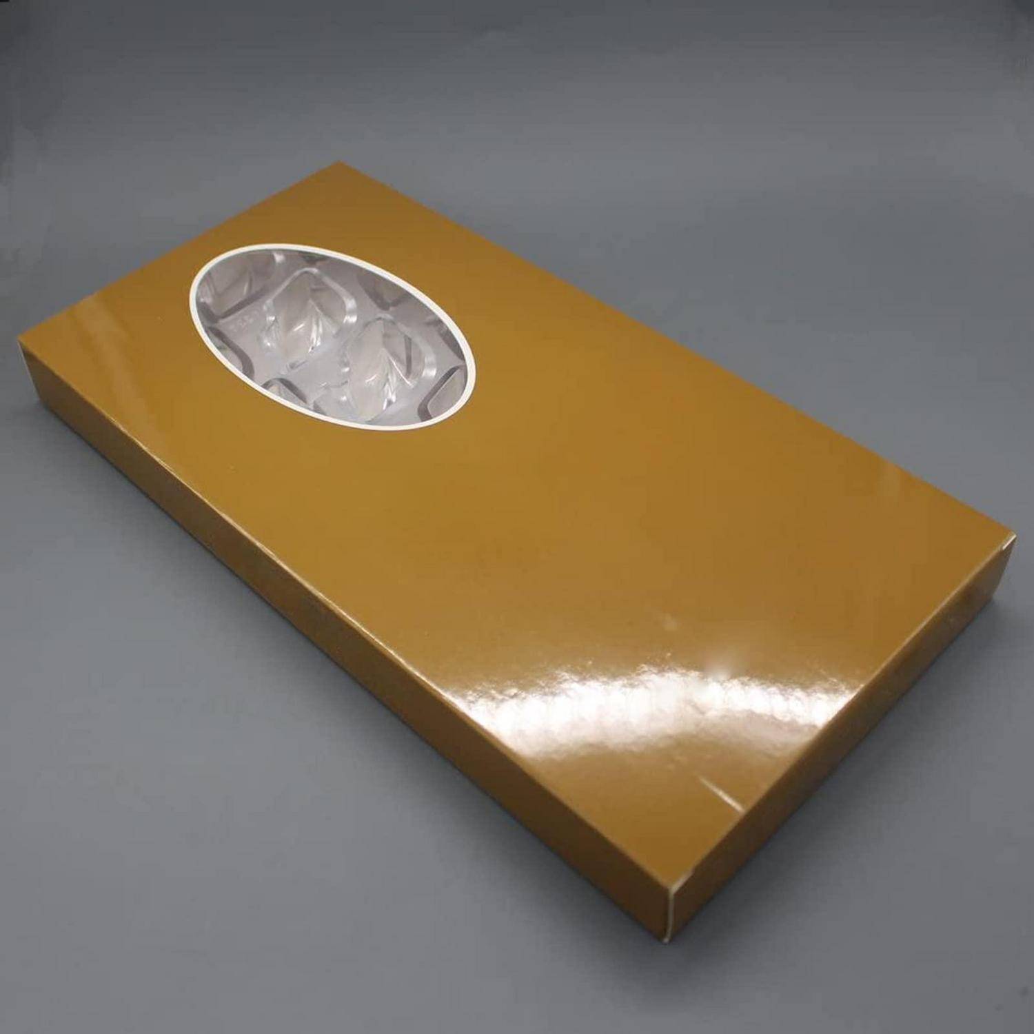 Goldene rechteckige Geschenkbox mit ovalem, transparentem Fenster, das weiße Seidenpapiere zeigt, auf einer grauen Oberfläche dargestellt.