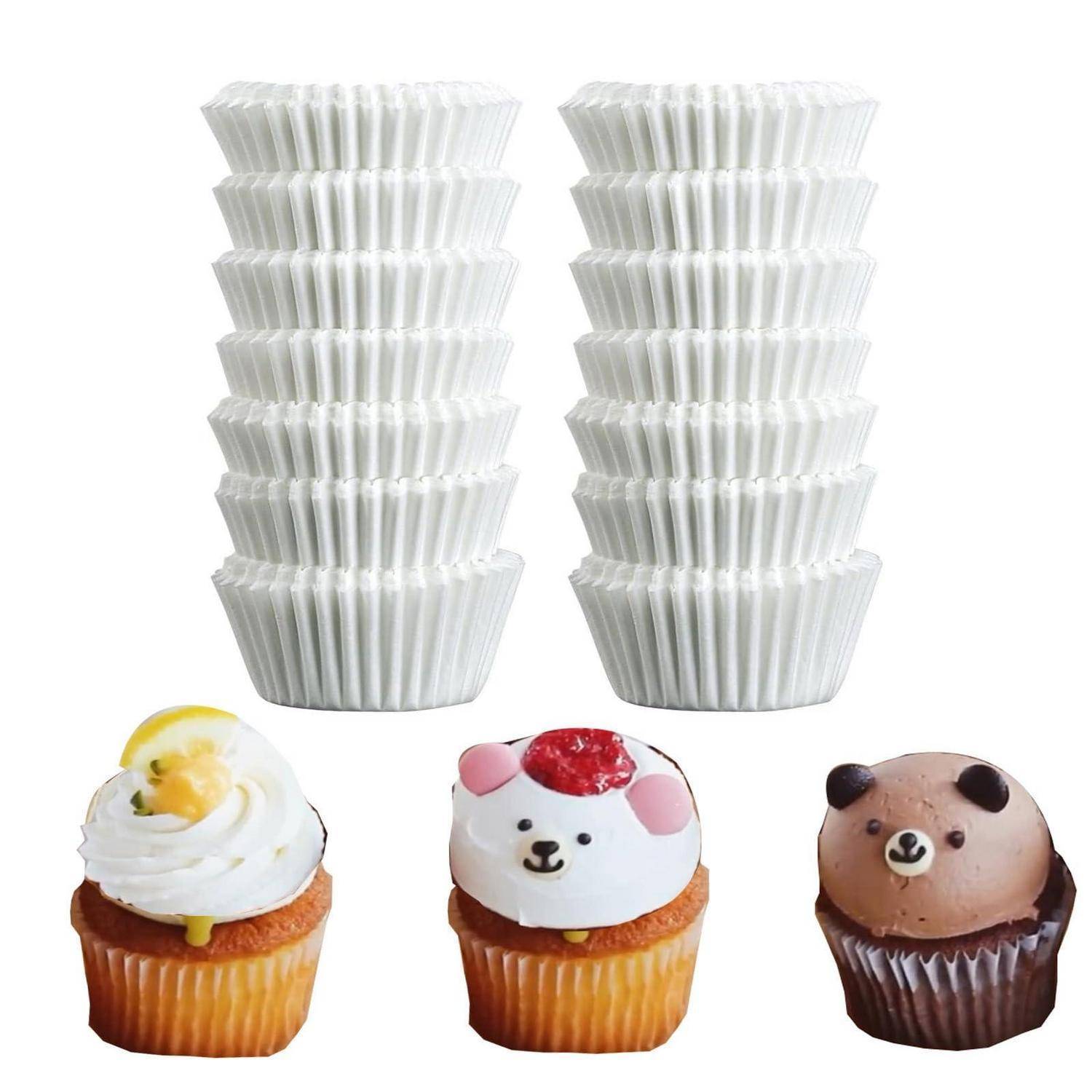 Zwei Stapel weißer Cupcake-Förmchen über drei dekorierten Cupcakes: einer mit weißem Frosting, ein Bärenkopf und ein Schokoladen-Bärenkopf.