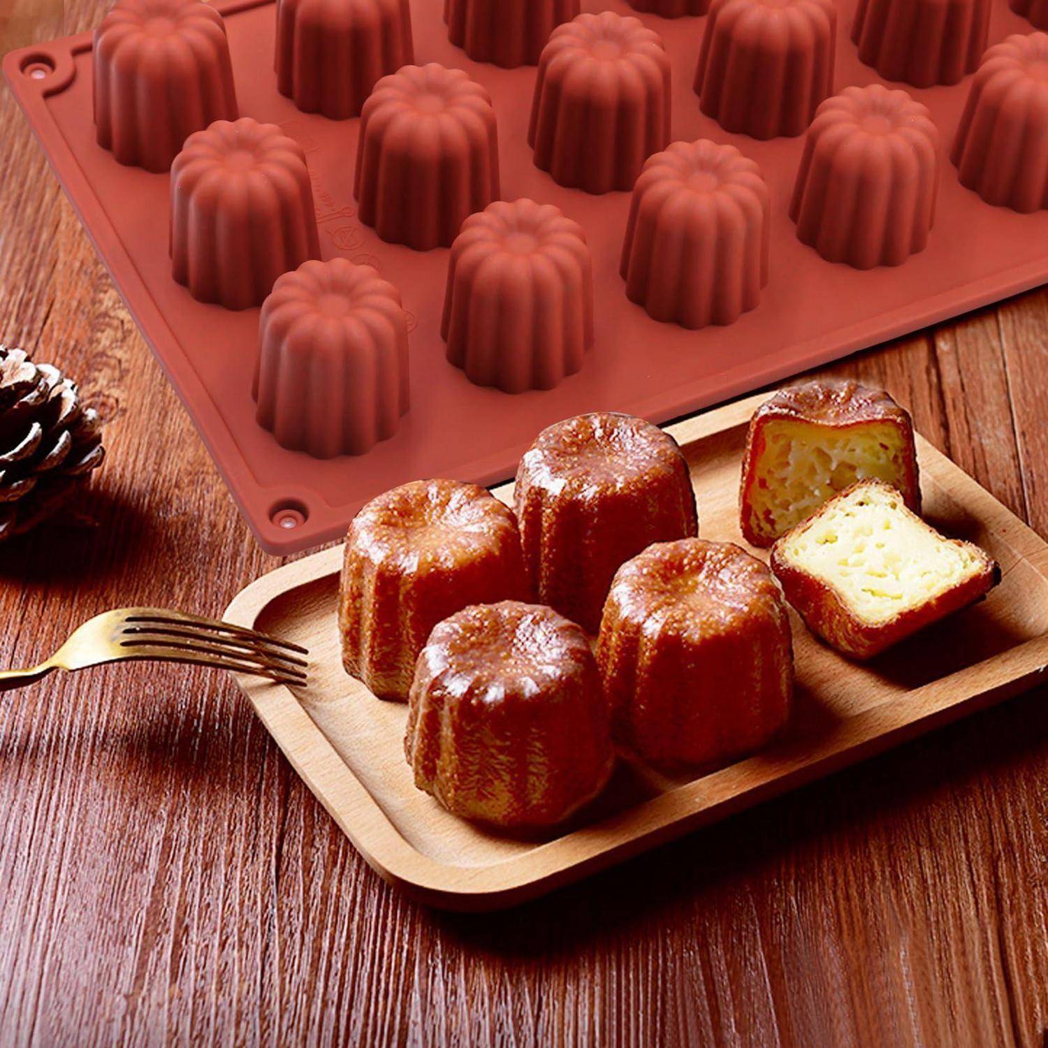 Canelé-Gebäck auf einem Holztablett neben einer Silikonform, mit einem aufgeschnittenen Exemplar, das das cremige Innere zeigt.