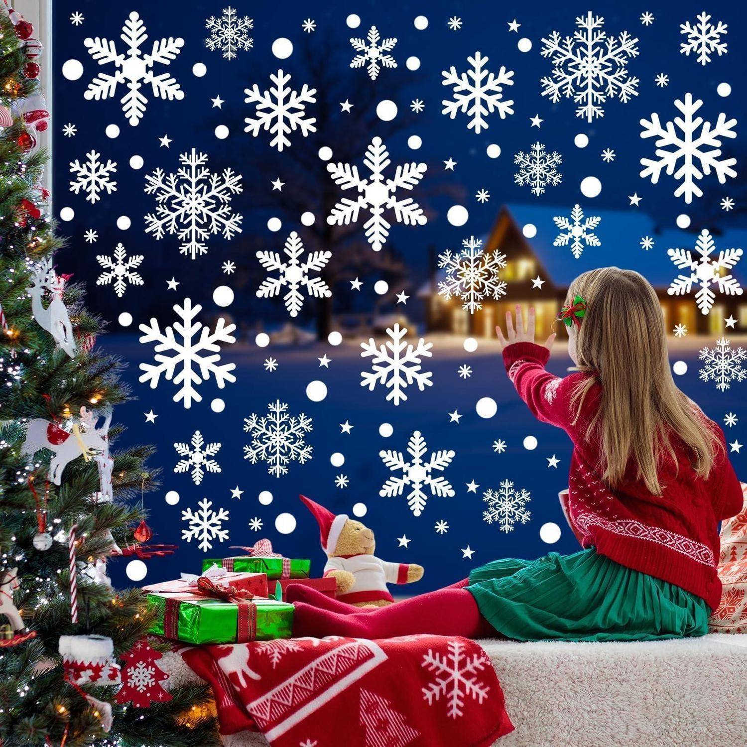 Ein junges Mädchen in einem roten Pullover und einem grünen Rock sitzt neben einem geschmückten Weihnachtsbaum und schaut auf eine verschneite Nachtszene mit Schneeflocken und einem beleuchteten Haus.