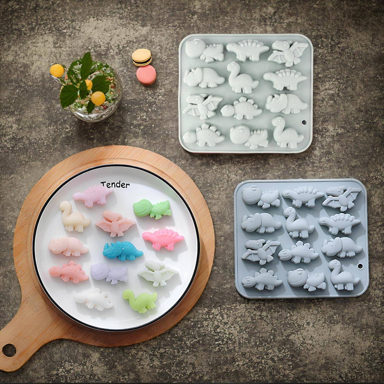 Draufsicht auf bunte tierförmige Bonbons auf einem runden "Tender""-Teller neben zwei Silikon-Gussformen auf einer Steinoberfläche.