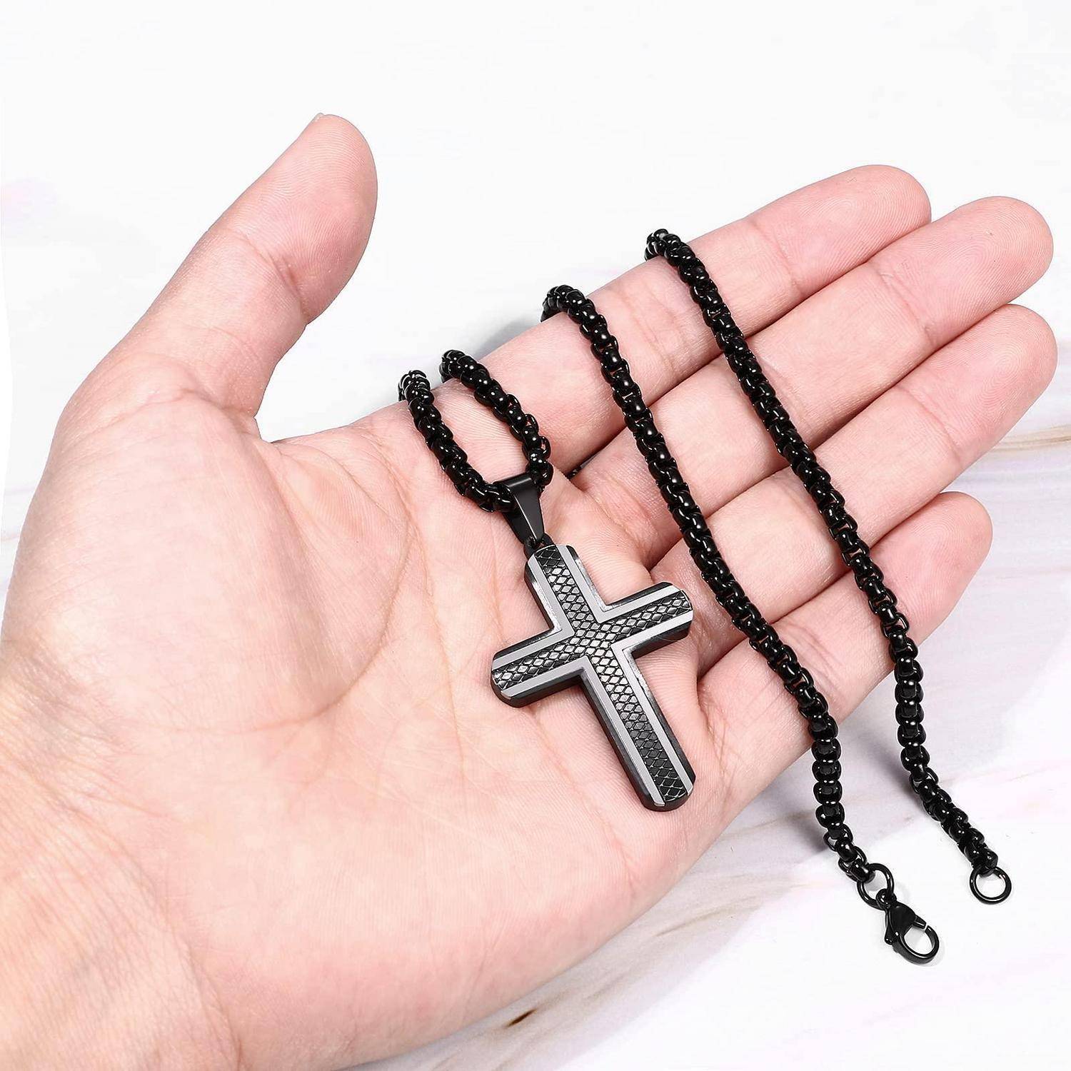 Eine Hand, die eine schwarze Perlenkette mit einem silbernen Kreuzanhänger auf weißem Hintergrund hält.