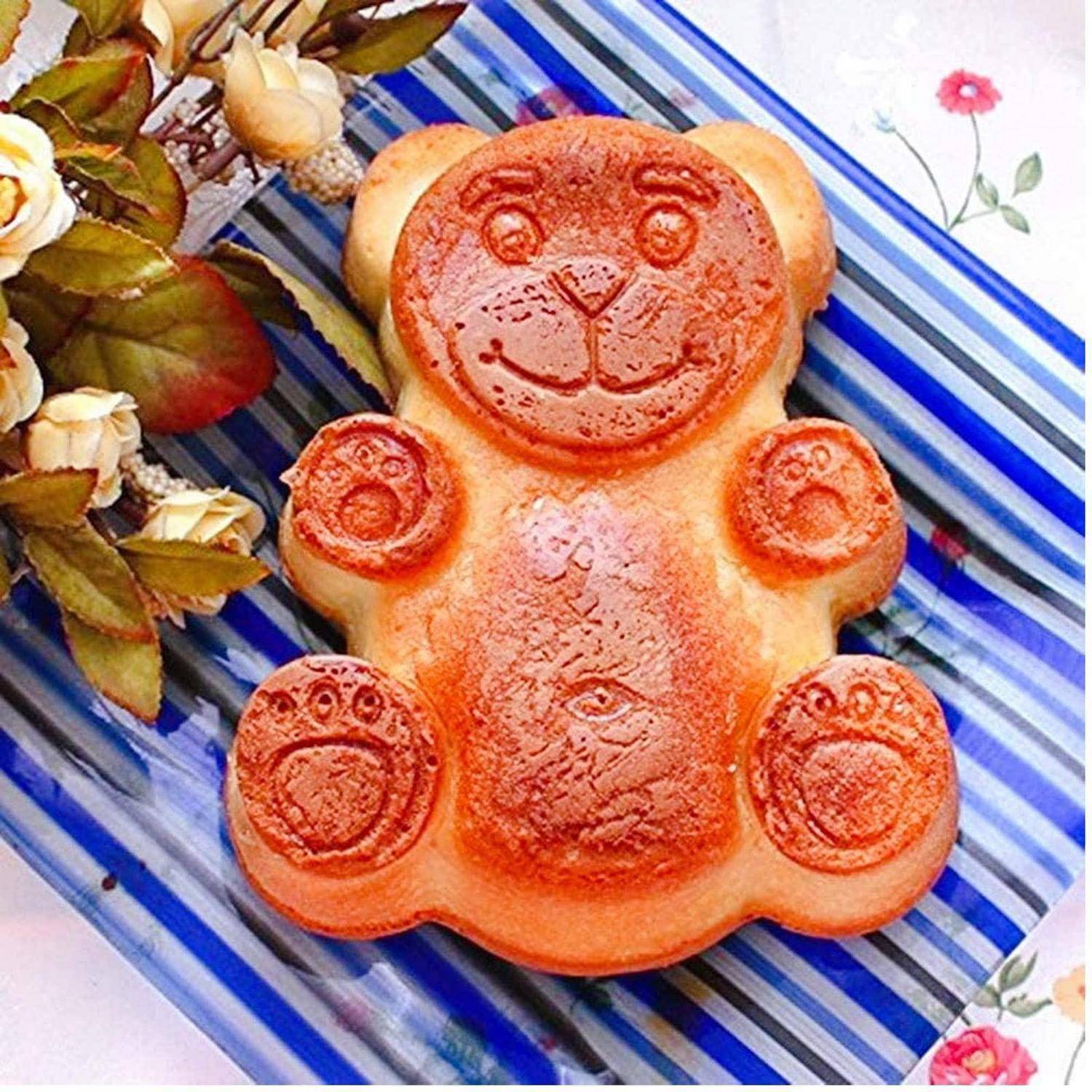 Bärenförmiger Kuchen oder Gebäck auf einem gestreiften Teller, umgeben von getrockneten Blumen.