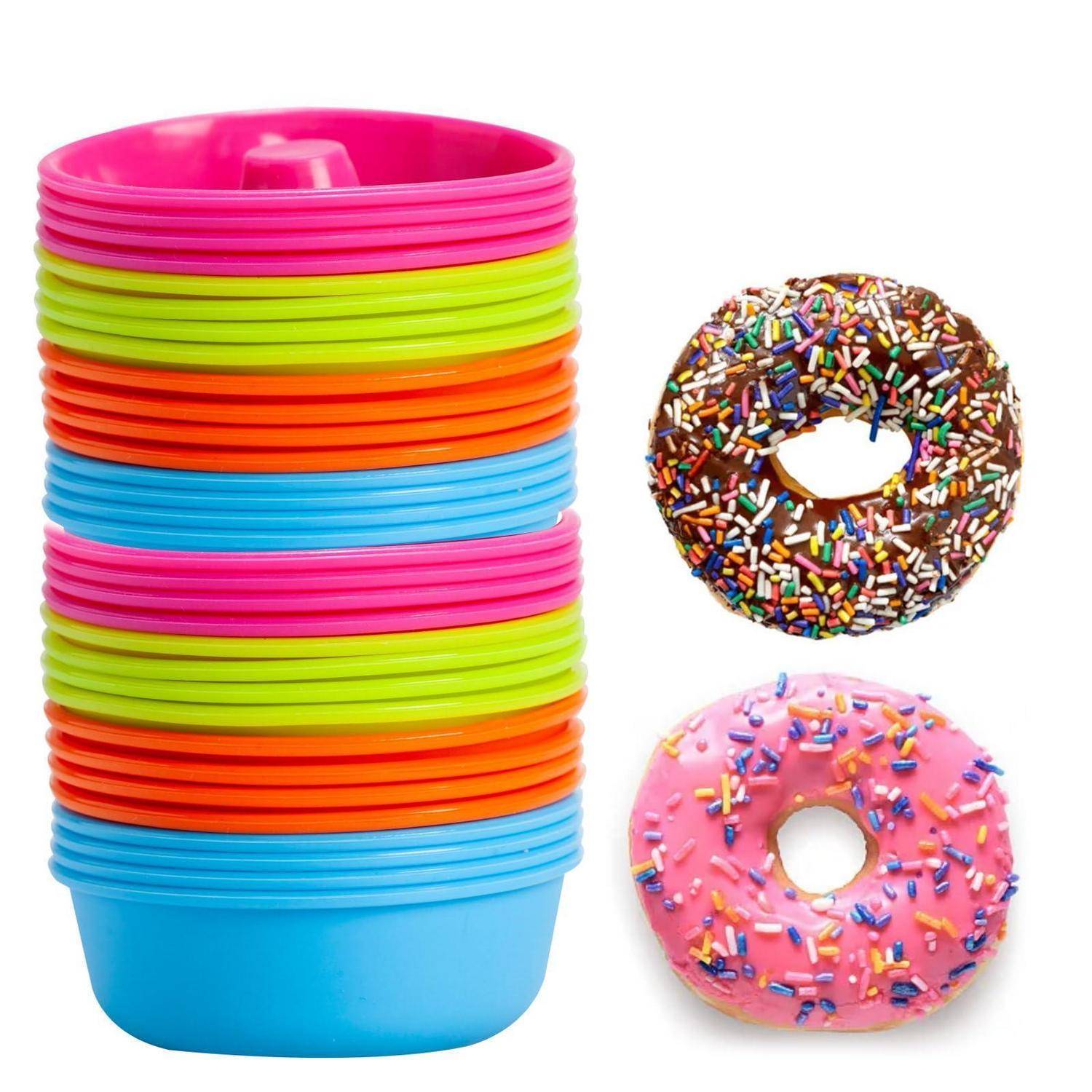 Bunter Stapel verschachtelter Kunststoffschüsseln neben zwei gestreuten Donuts, einer Schokoladen- und einer rosa, auf weißem Hintergrund.