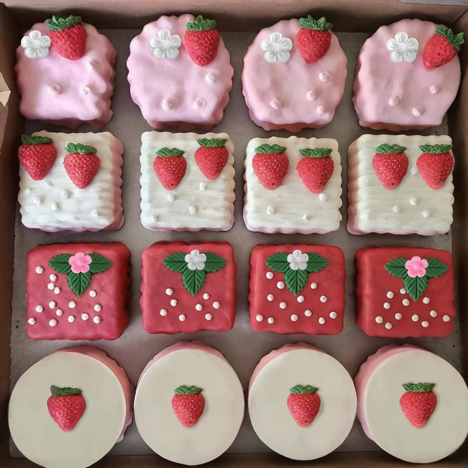 Tablett mit dekorierten Erdbeerkeksen, angeordnet in vier Reihen, mit rosa, weißen, roten und runden glasierten Designs, belegt mit Erdbeeren und Blumen.