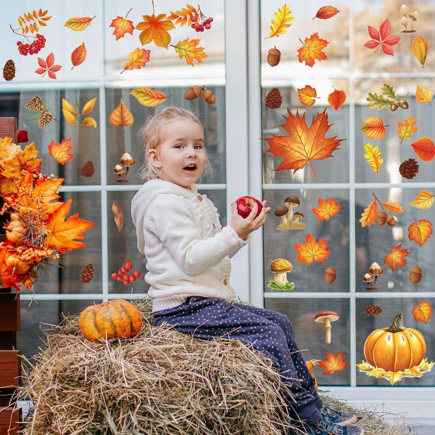 Ein kleines Kind sitzt auf Heu und hält einen Apfel in der Hand, umgeben von Herbstblättern, Kürbissen, Eicheln und Pilzen in einer herbstlichen Außenausstellung.