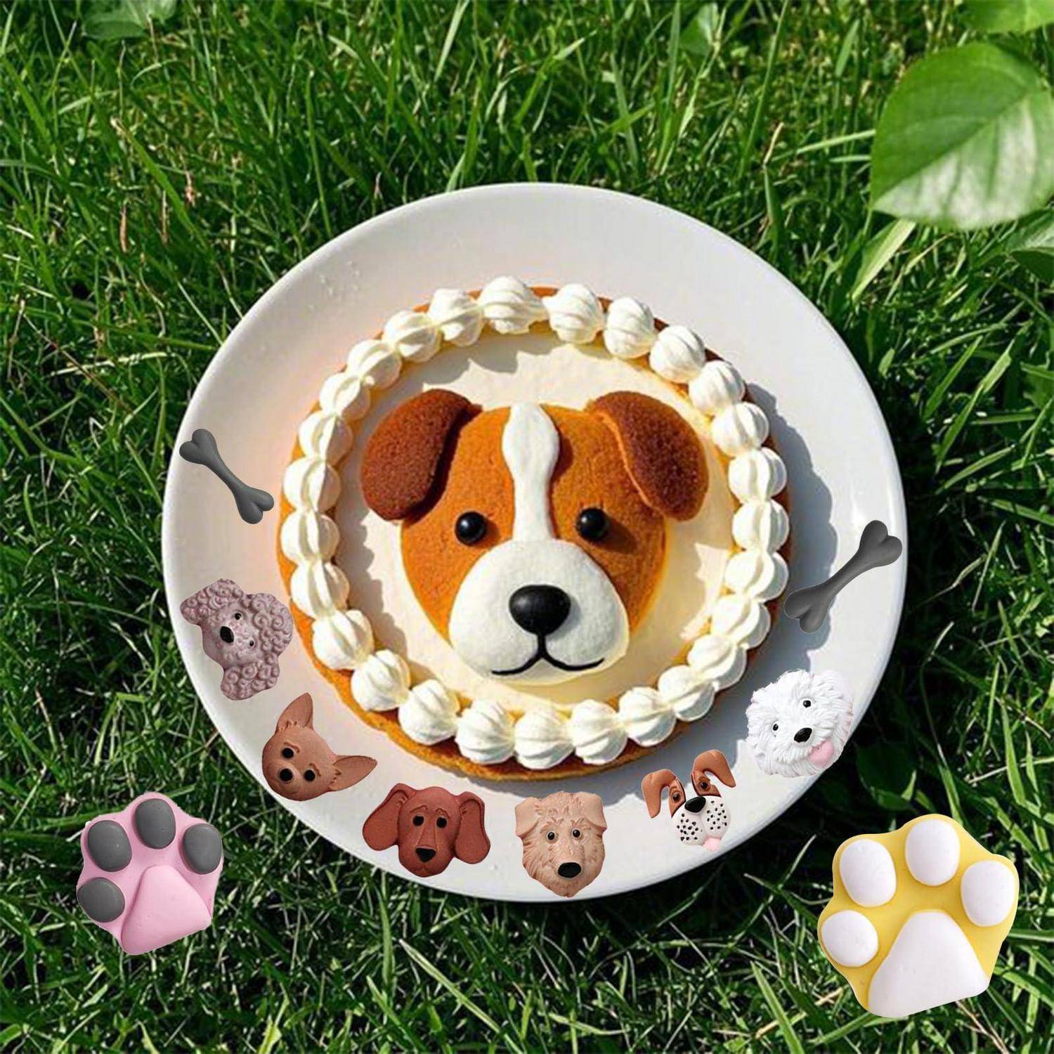 Hundemotiv-Kuchen auf einem weißen Teller, dekoriert wie ein Welpengesicht mit Pfotenzier, auf Gras stehend.