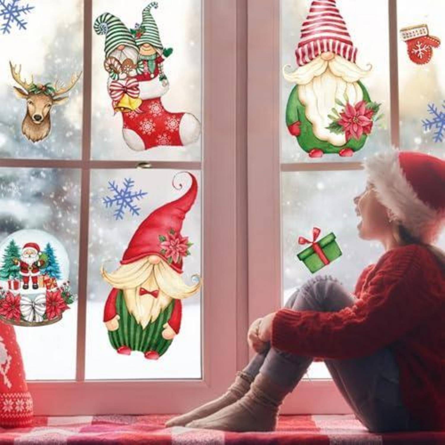 Ein Mädchen in einer Weihnachtsmütze sitzt an einem Fenster und betrachtet weihnachtliche Aufkleber von Gartenzwergen, einem Rentier, einem Strumpf und Geschenken auf mattiertem Glas.