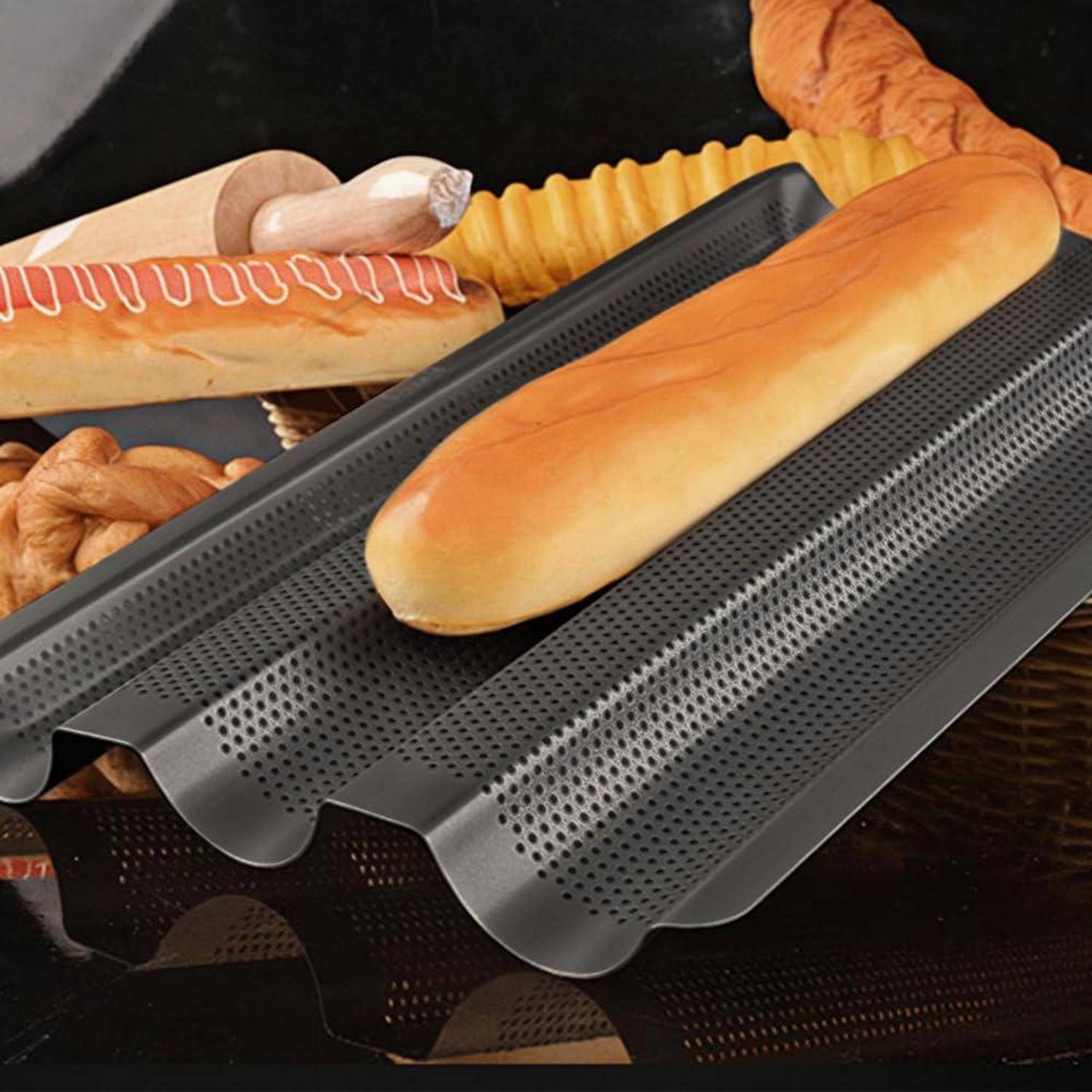 Durchbrochenes Backblech mit langem Brotlaib, gezeigt mit gebackenen Baguettes im Hintergrund auf einer dunklen Oberfläche.