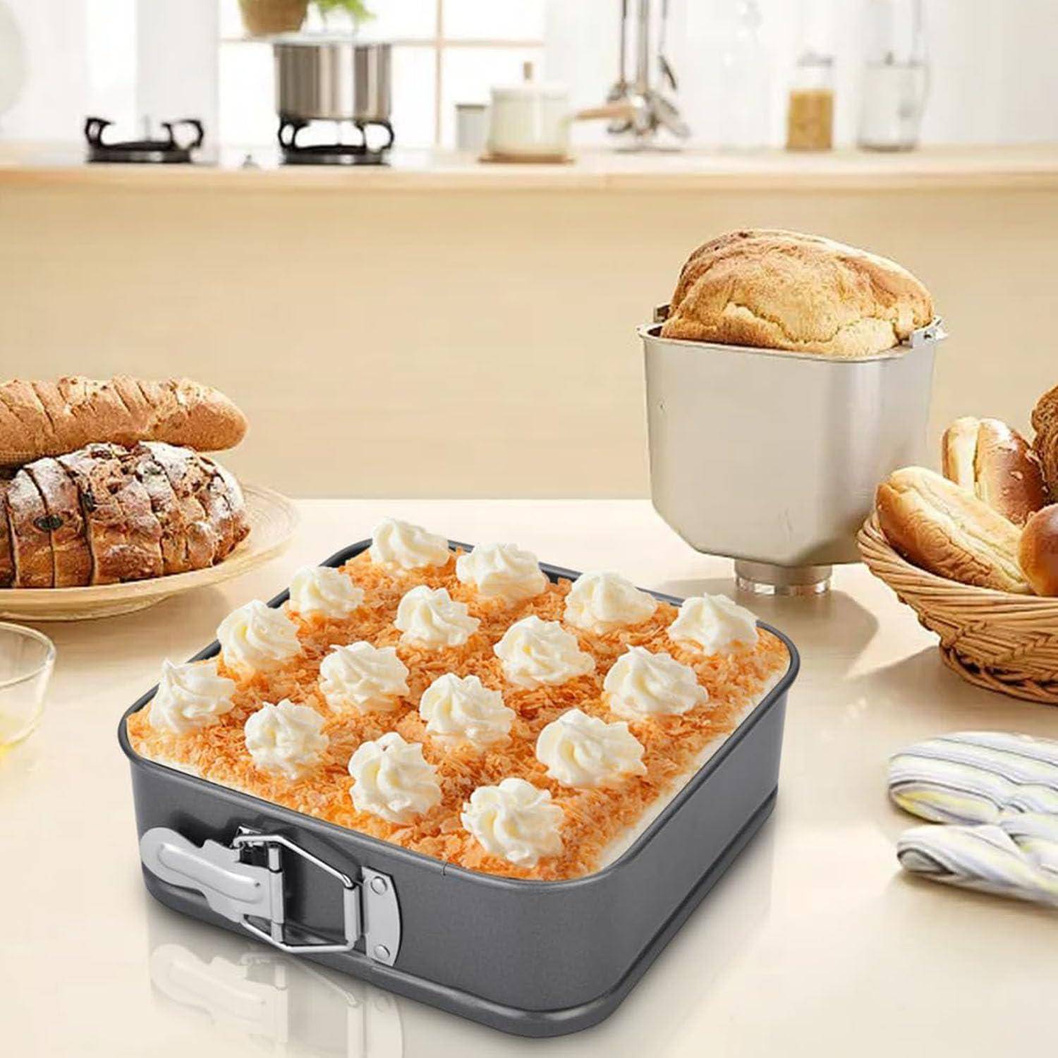 Quadratische Springform gefüllt mit einem Dessert, das mit Schlagsahne bedeckt ist, umgeben von Brot und Gebäck auf einer Küchentheke.