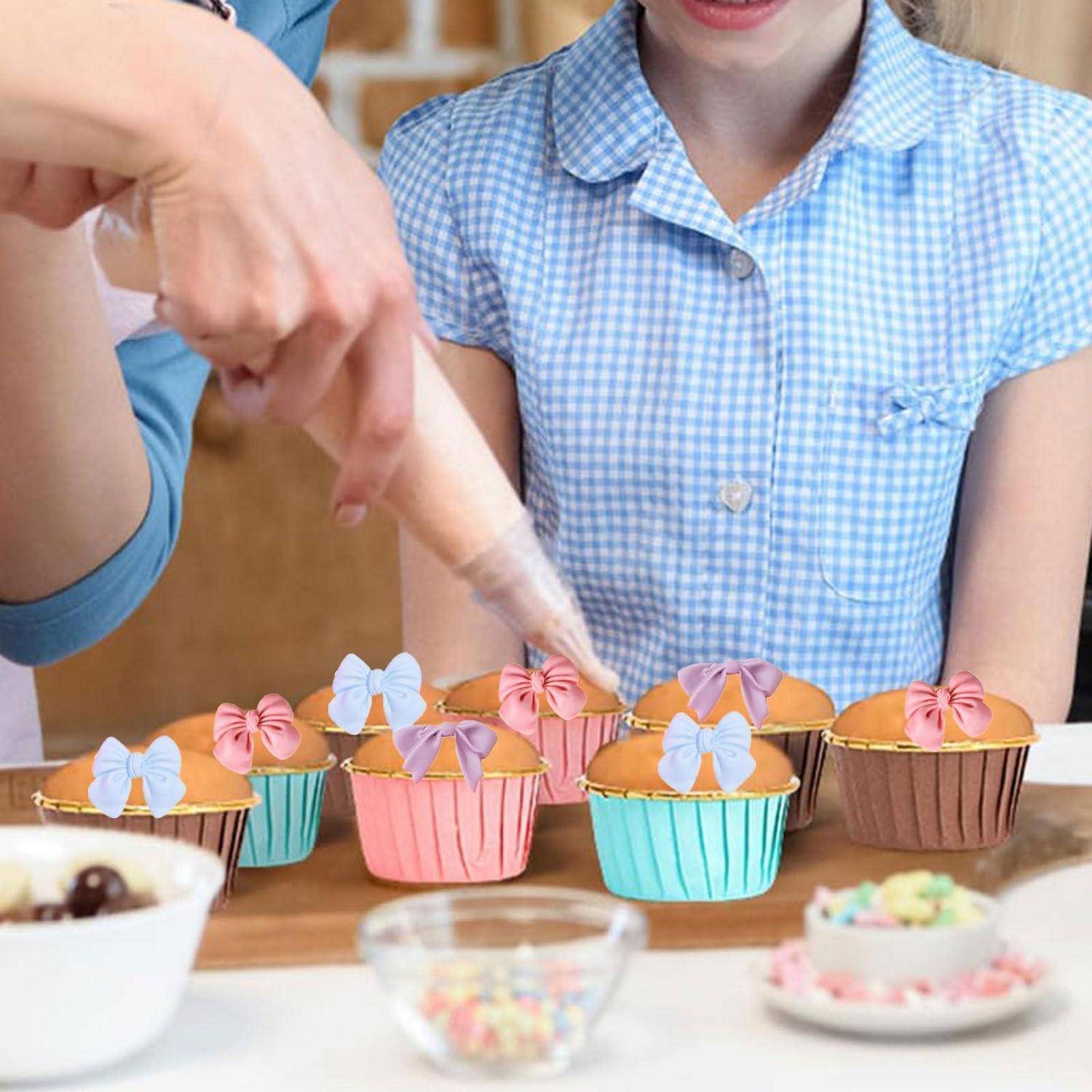 Eine Person spritzt Zuckerguss auf bunte Cupcakes, während ein Kind in einem blauen karierten Hemd an einem Backtisch zusieht.