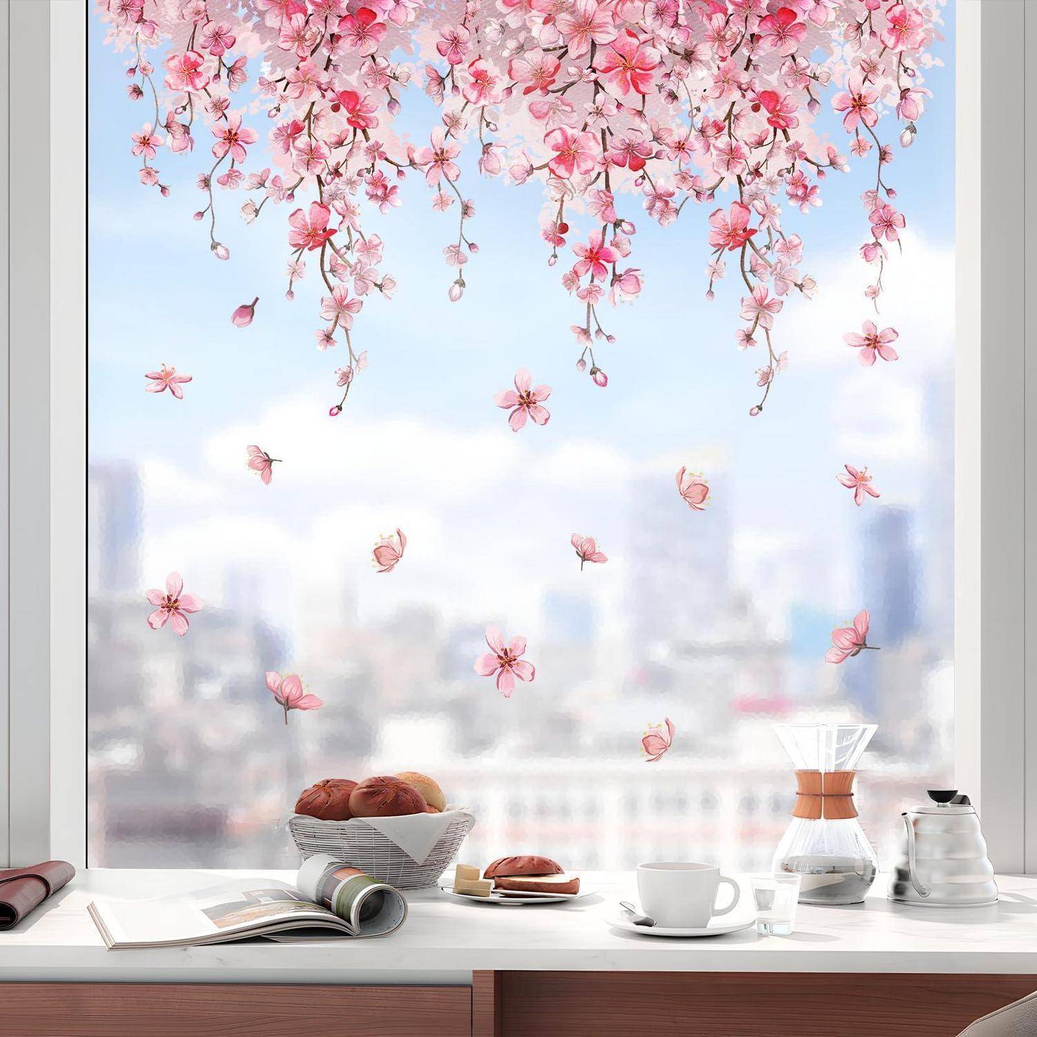Kirschblütenzweige rahmen ein helles Fenster über einem Frühstückstisch mit Gebäck, Kaffee, Zeitschriften und einer Stadtaussicht dahinter.