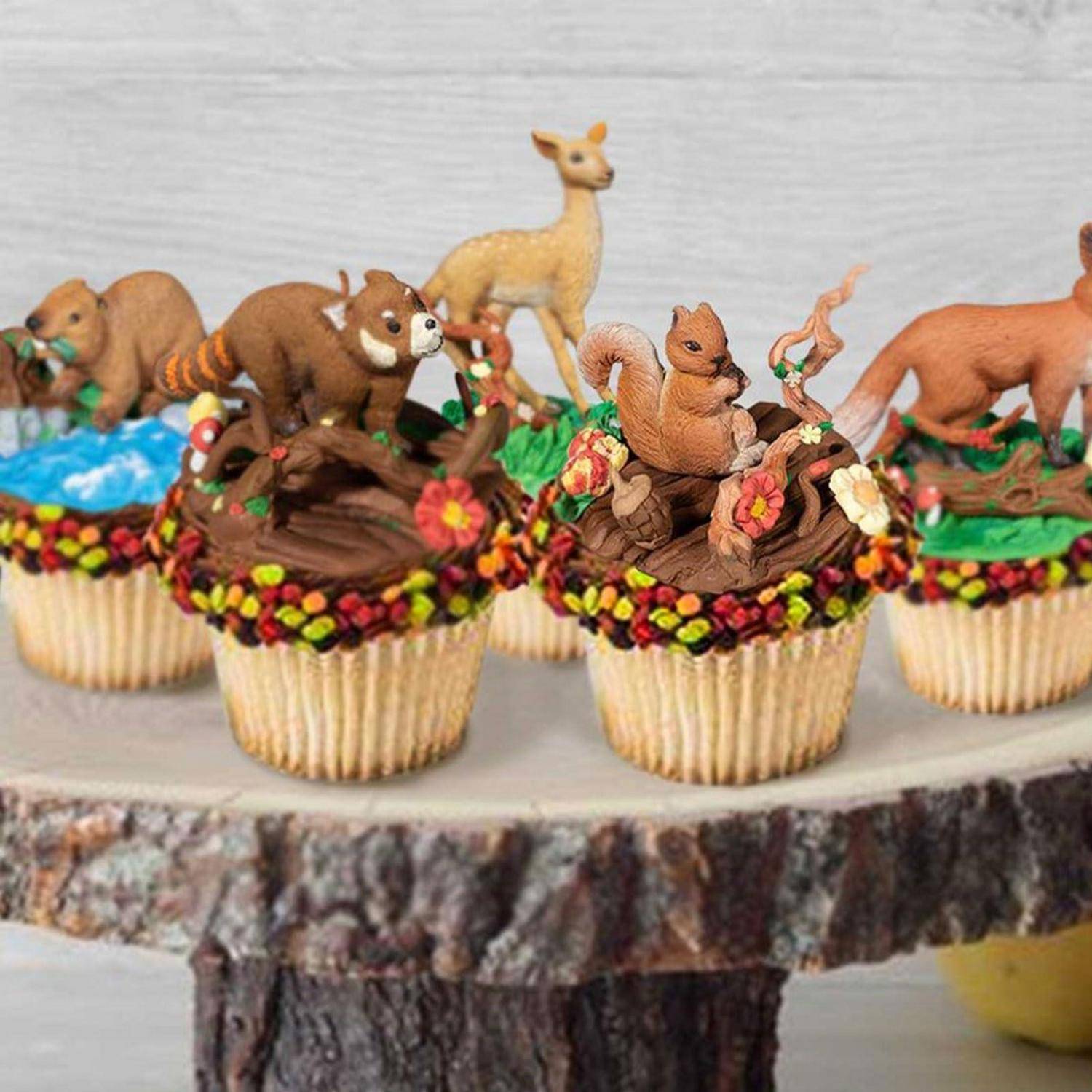 Tier-förmig angeordnete Cupcakes mit Tiermotiven, verziert mit Waldtieren wie Eichhörnchen, Rehen und Bären auf einem rustikalen Kuchenständer.