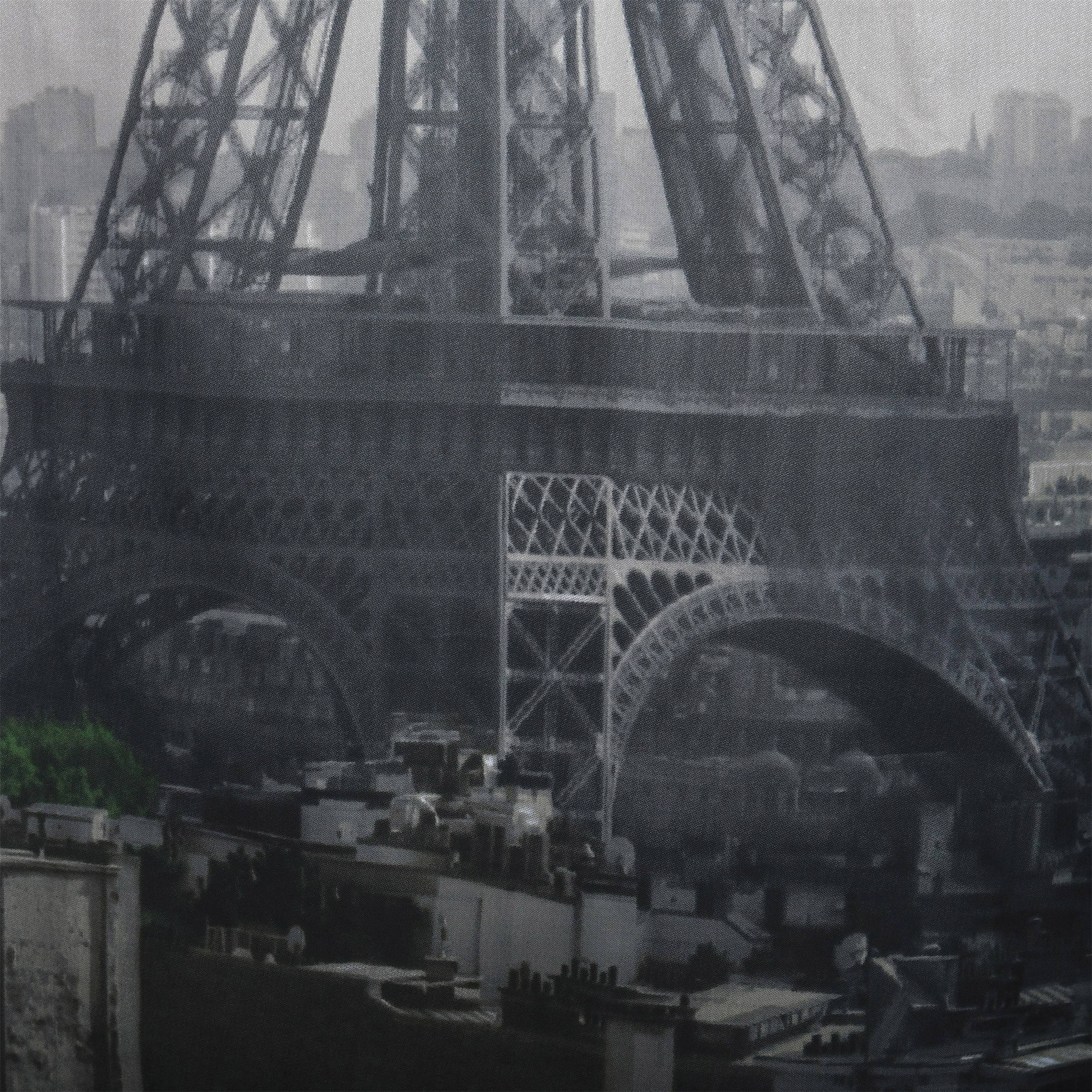 Eiffel-Turm-Basis und untere Bögen in einer nebligen Ansicht über nahegelegene Gebäude und Dächer.