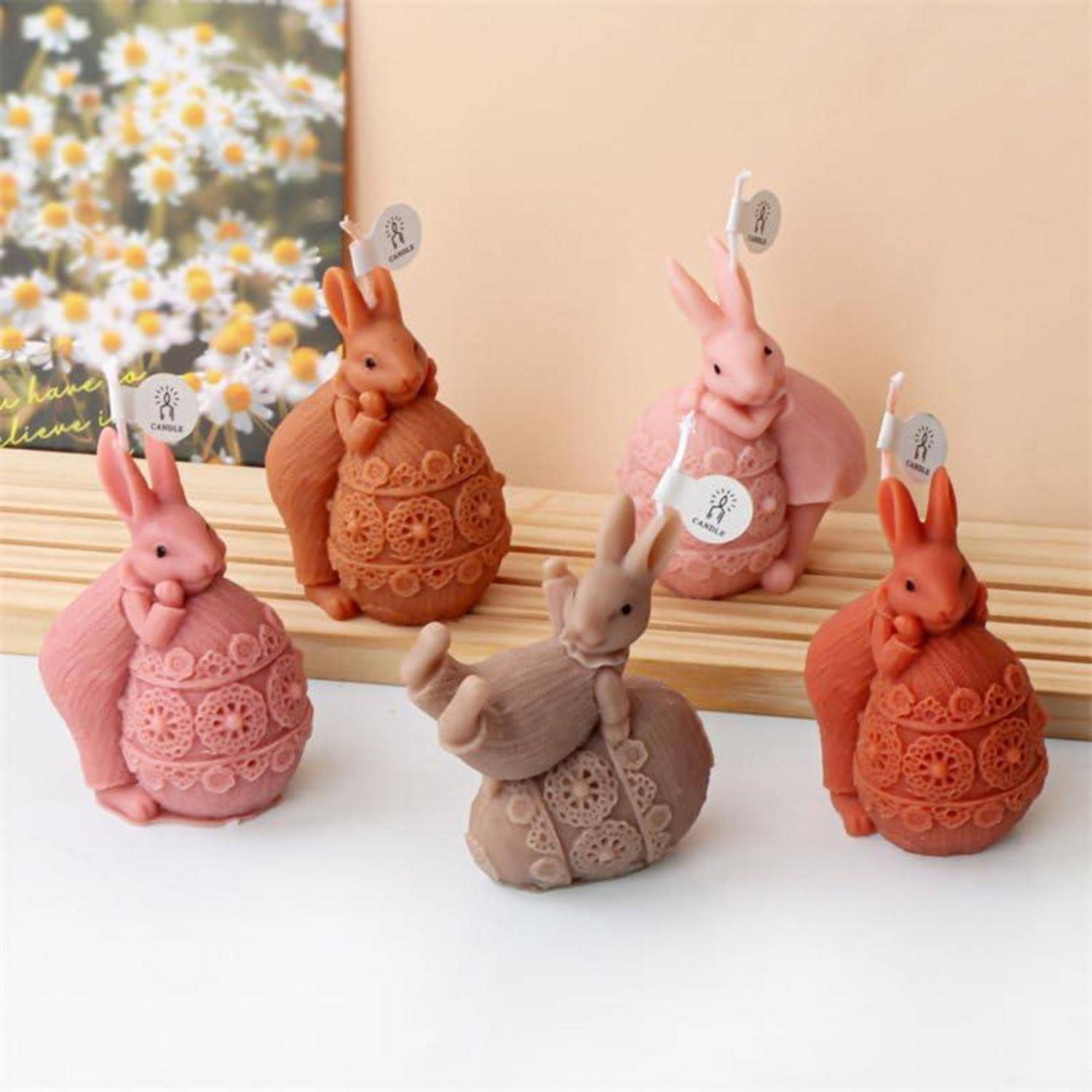 Fünf dekorative Kaninchenfiguren in Rosa, Orange und Beige, arrangiert auf einer weißen Oberfläche vor einem blumigen Hintergrund.