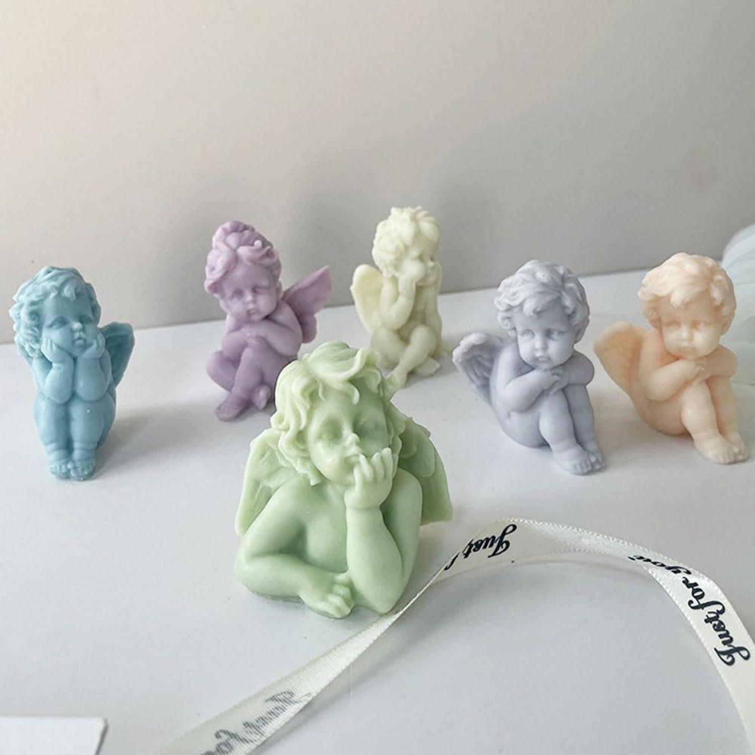 Pastellfarbene Cherub-Figürchen in Blau, Lila, Grün, Gelb, Grau und Pfirsich, angeordnet auf einer weißen Oberfläche mit einem 