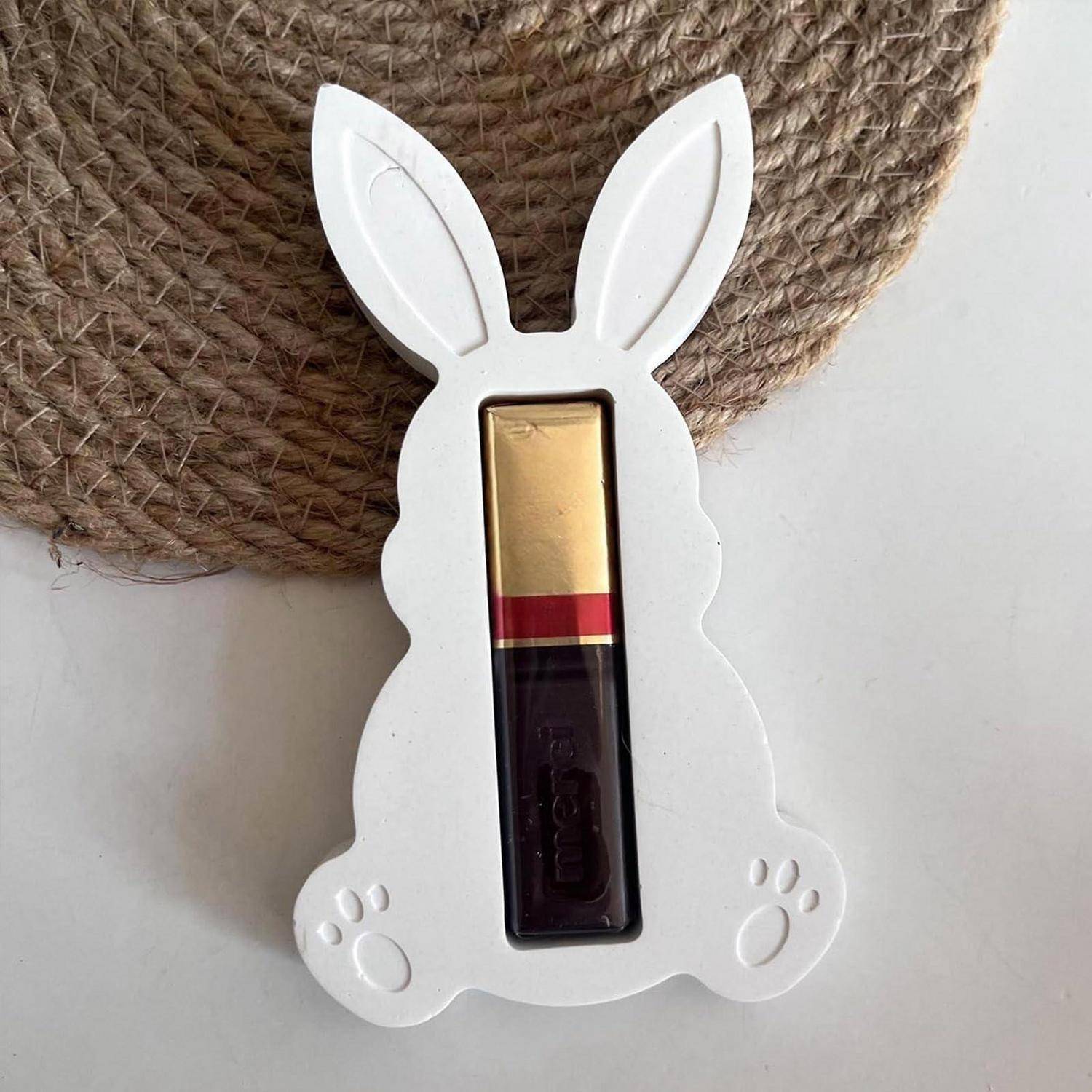 Weißer Halter in Hasenform mit rechteckiger Öffnung, der einen Lippenbalsam-Behälter zeigt, auf einer weißen Oberfläche neben einem gewebten Untersetzer.
