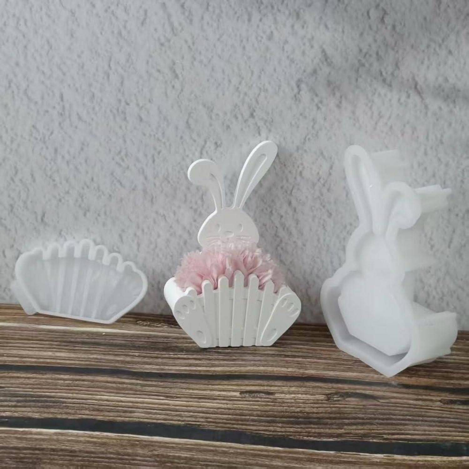Weiße Osterhasen-Dekorationen auf einem Holzregal, darunter ein Hase in einem muschelförmigen Halter und eine weitere Hasenfigur rechts.