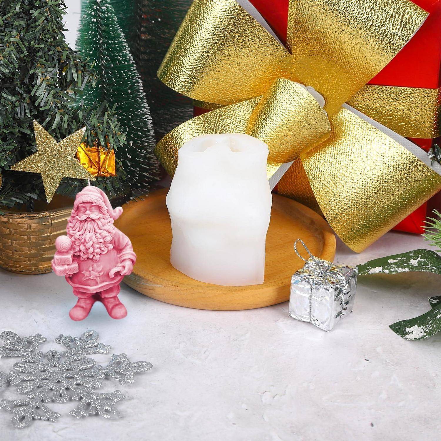 Weiße Kerze auf einem Holztablett mit Weihnachtsdekoration: rosa Weihnachtsmannfigur, Minibaum, Geschenkbox, goldene Schleife und silberner Schneeflockenanhänger.