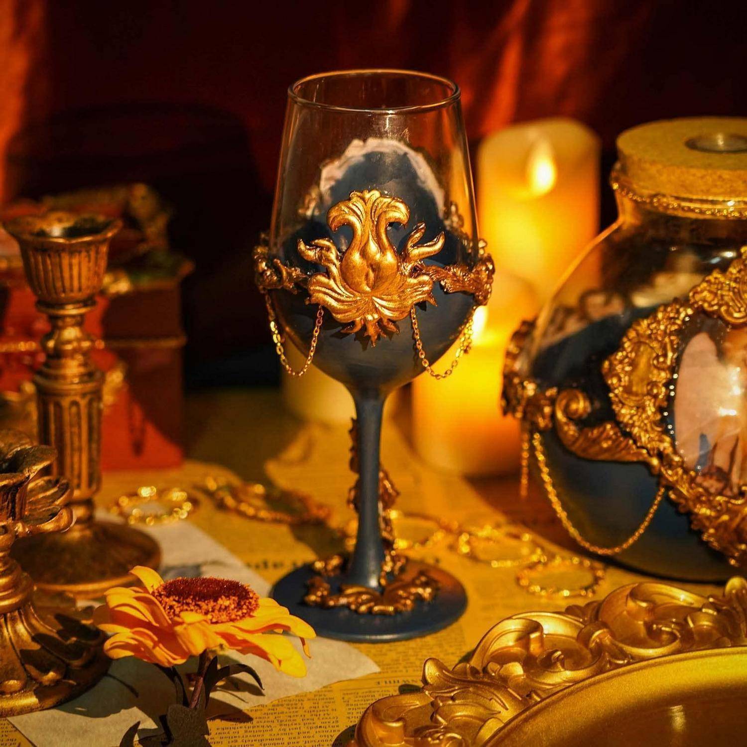 Verzierter dunkelblauer Kelch mit goldener Filigranarbeit auf einem Tisch mit Kerzen, Goldmünzen und dekorativen Objekten im warmen Licht.