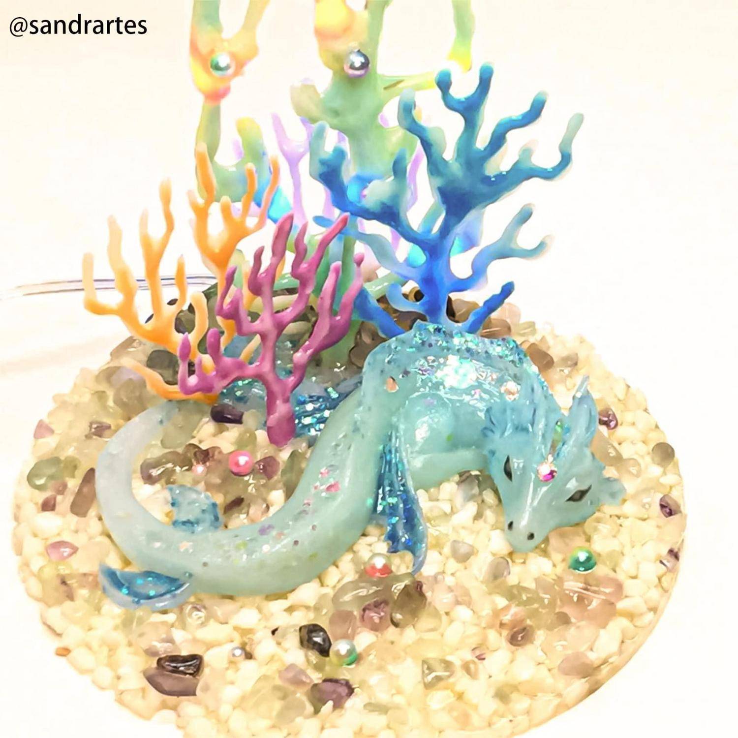 Eine durchscheinende blaue Drachenfigurine ruht auf einem Kieselsteinsockel inmitten bunter korallenähnlicher Dekorationen und schafft eine Unterwasser-themenbezogene Ausstellung.