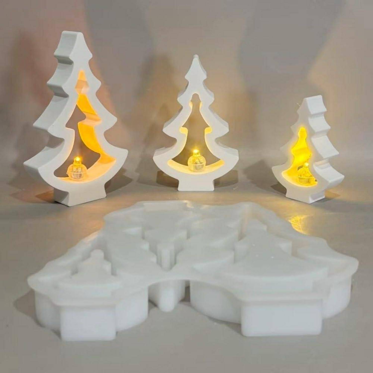 Weiße Weihnachtsbaumförmige Kerzenhalter mit leuchtend gelben Lichtern, plus eine größere weiße baumförmige Form oder Basis im Vordergrund.
