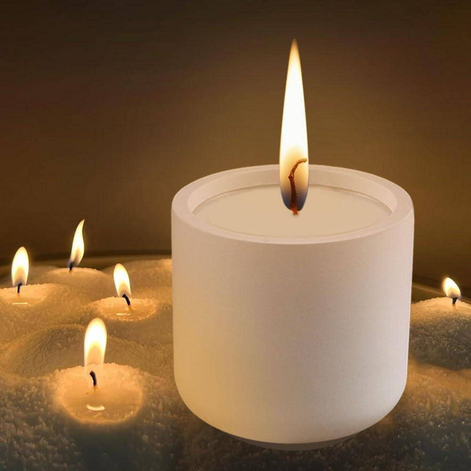 Weiße zylindrische Kerze, die in einem Sandbett brennt, mit mehreren kleineren brennenden Kerzen, die um sie herum glühen.