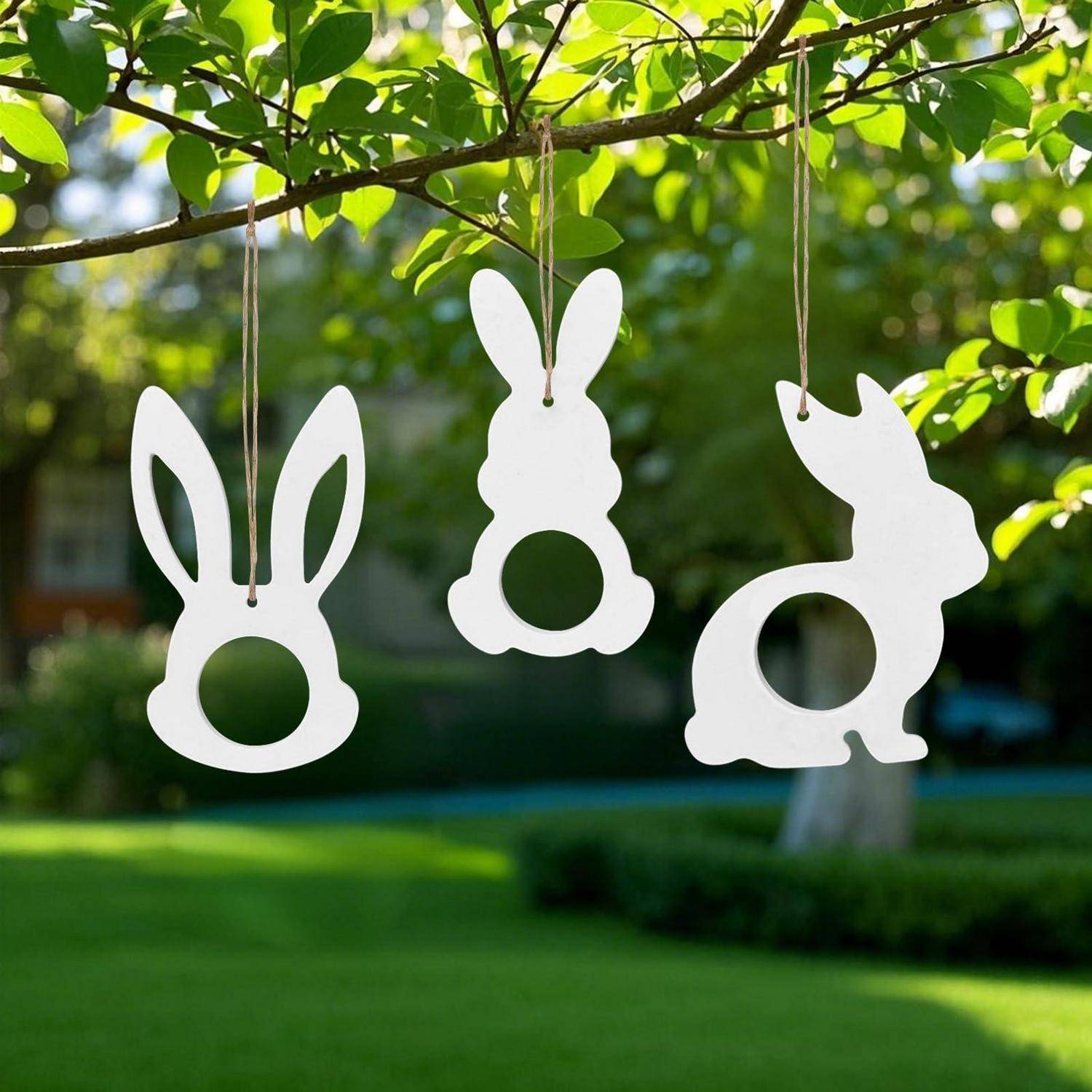 Drei weiße hasenförmige Hängekugeln baumeln von einem Baumast im Freien vor einem unscharfen grünen Gartenhintergrund.