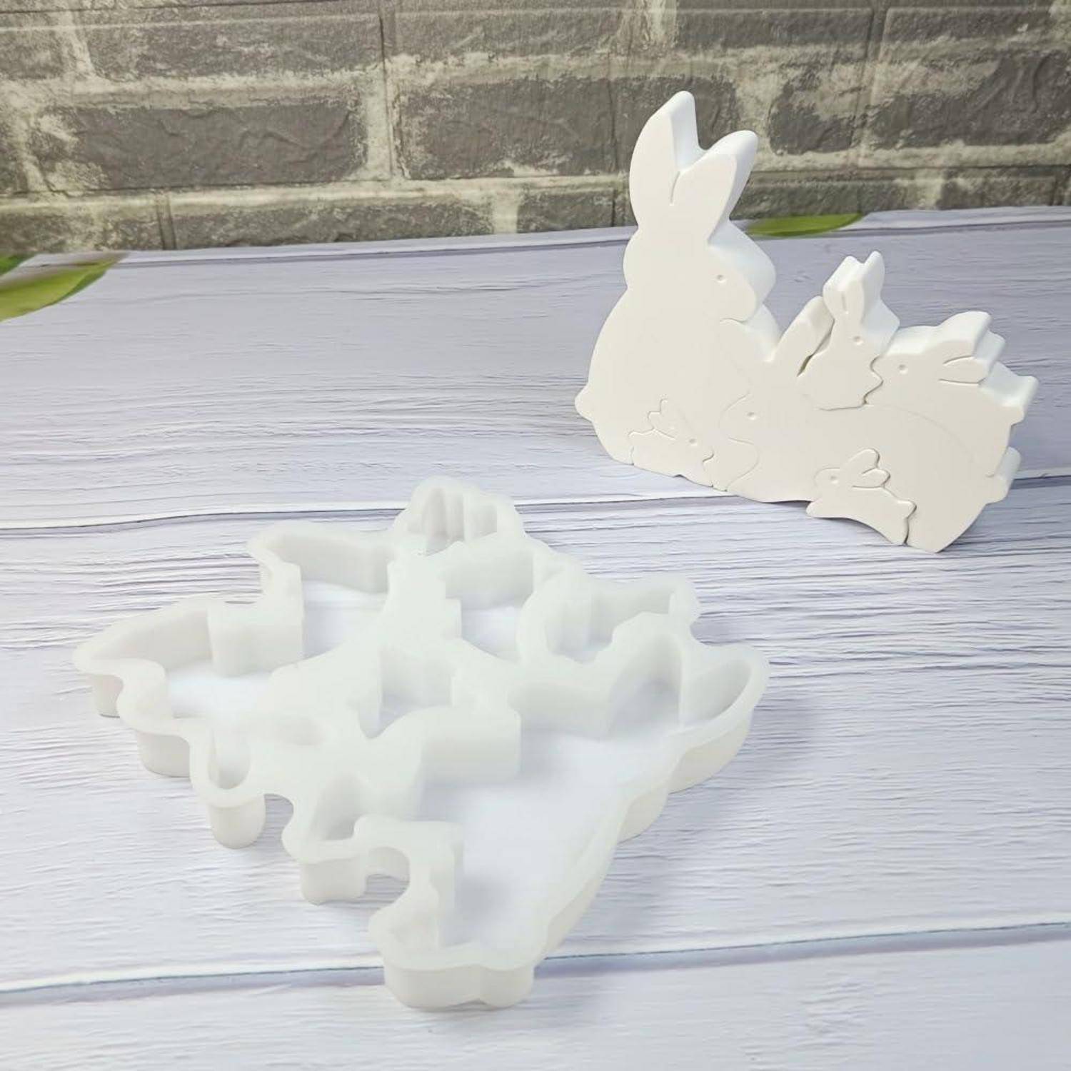 Zwei weiße kaninchenförmige Puzzleteile: ein flaches Stück vorne und ein zusammengesetztes stehendes Stück dahinter auf einer Holzoberfläche.