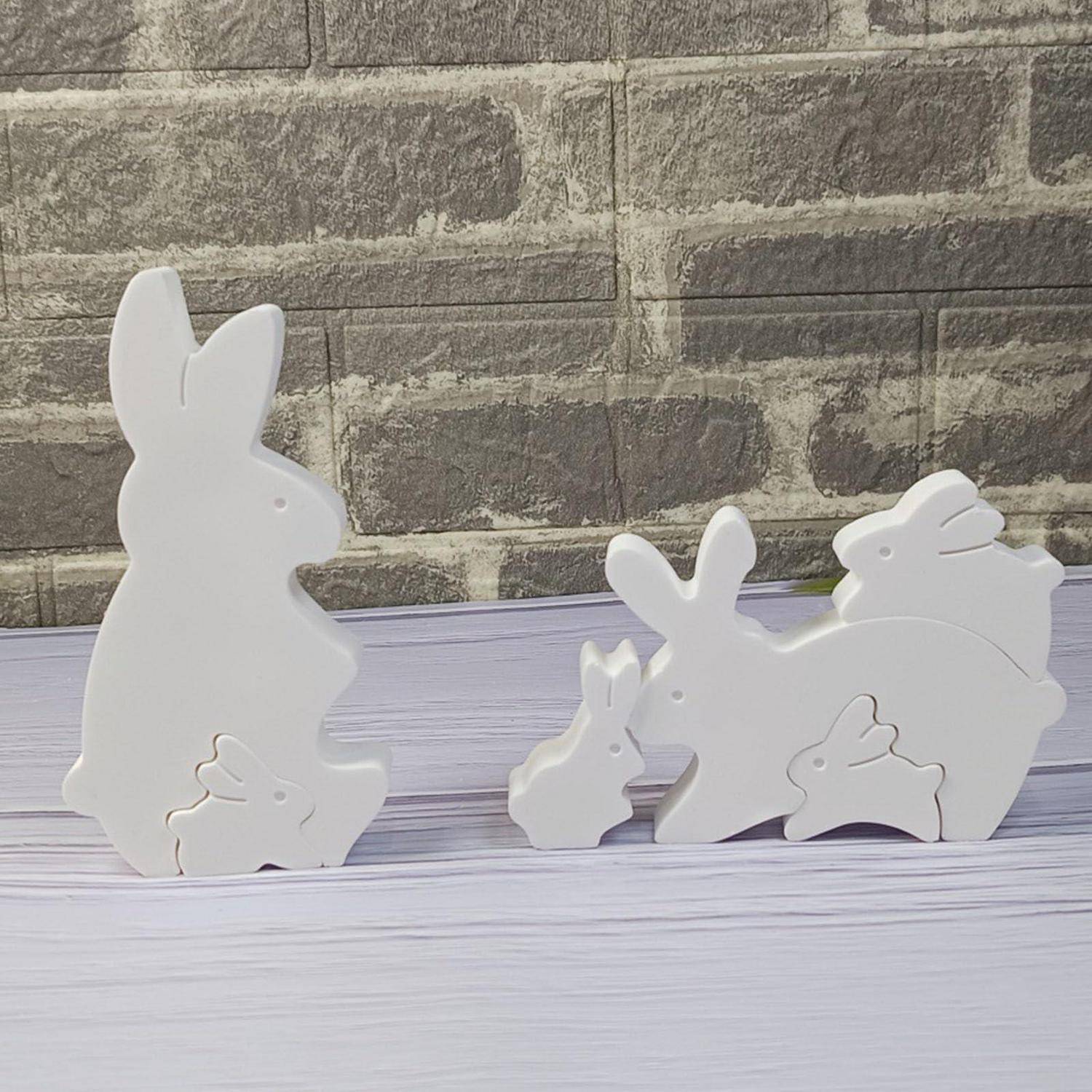 Weiße hölzerne Osterhase-Ausschnitte in verschiedenen Größen, angeordnet auf einer hellen Holzoberfläche vor einem Backsteinmauer-Hintergrund.