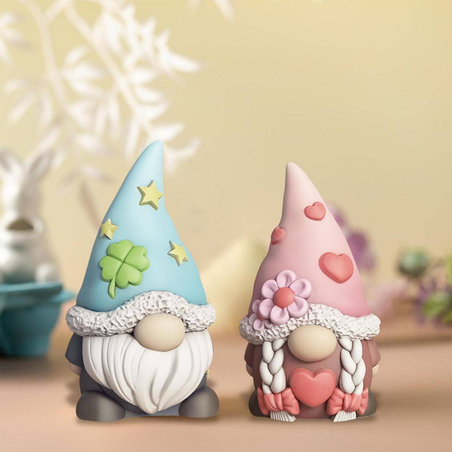 Zwei dekorative Gnomelfiaurinen, eine blaue mit Sternen und einem Kleeblatt, eine rosa mit Herzen und Blumen, nebeneinander stehend.