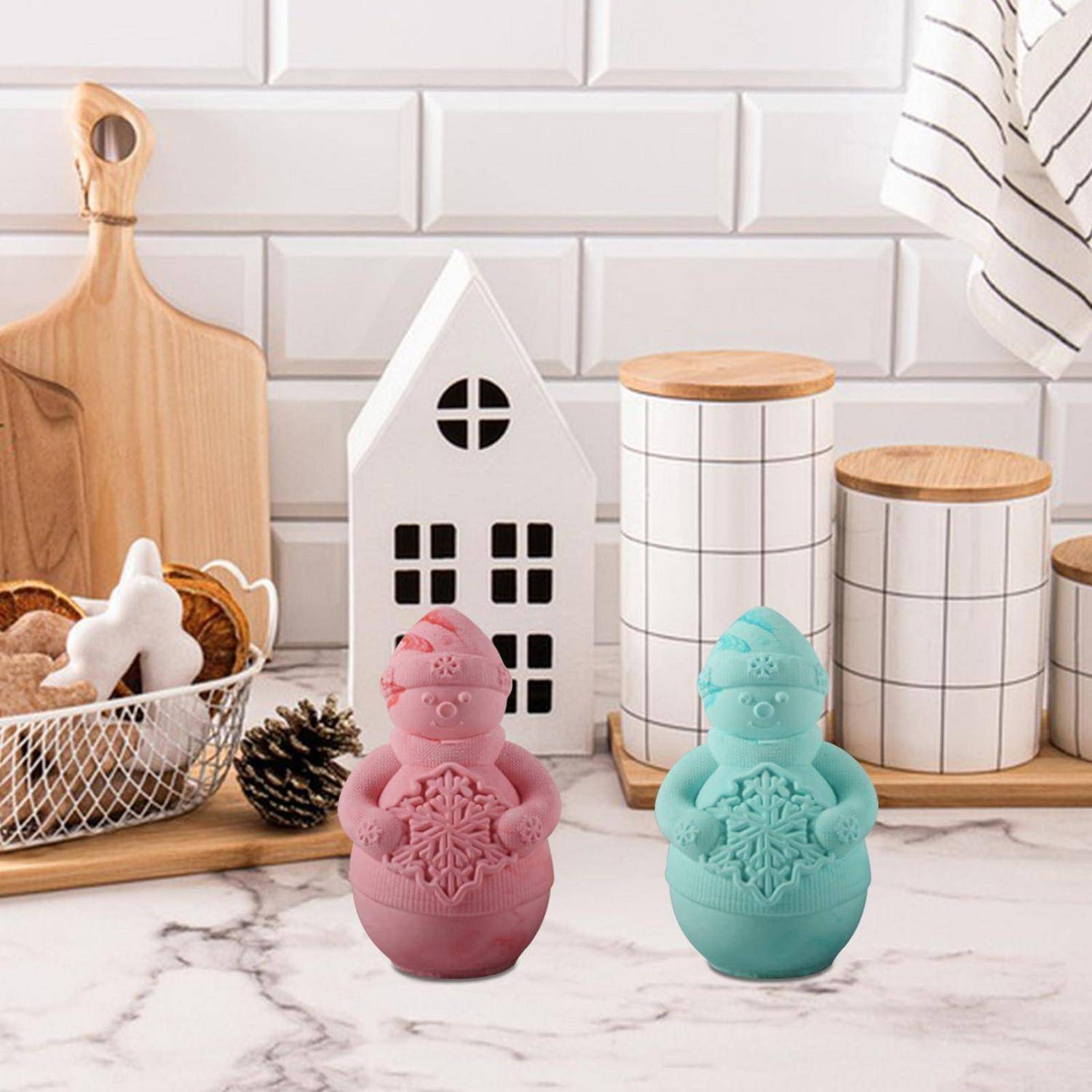 Zwei dekorative eiförmige Behälter, einer rosa und einer in Blaugrün, in Form von Häschen geformt, auf einer Küchentheke mit Holzbrettern und Behältern ausgestellt.