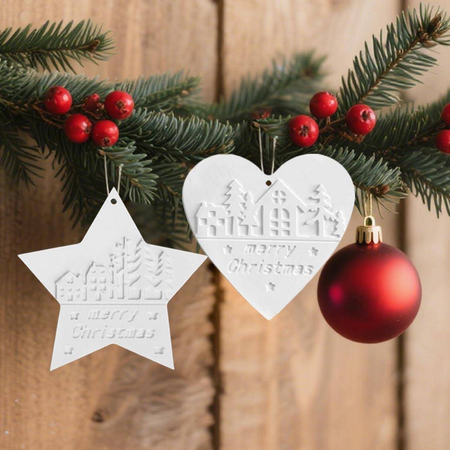 Weihnachtsdekoration mit Kiefernzweigen, roten Beeren, einer roten Christbaumkugel und zwei weißen hängenden Ornamenten mit der Aufschrift „Frohe Weihnachten