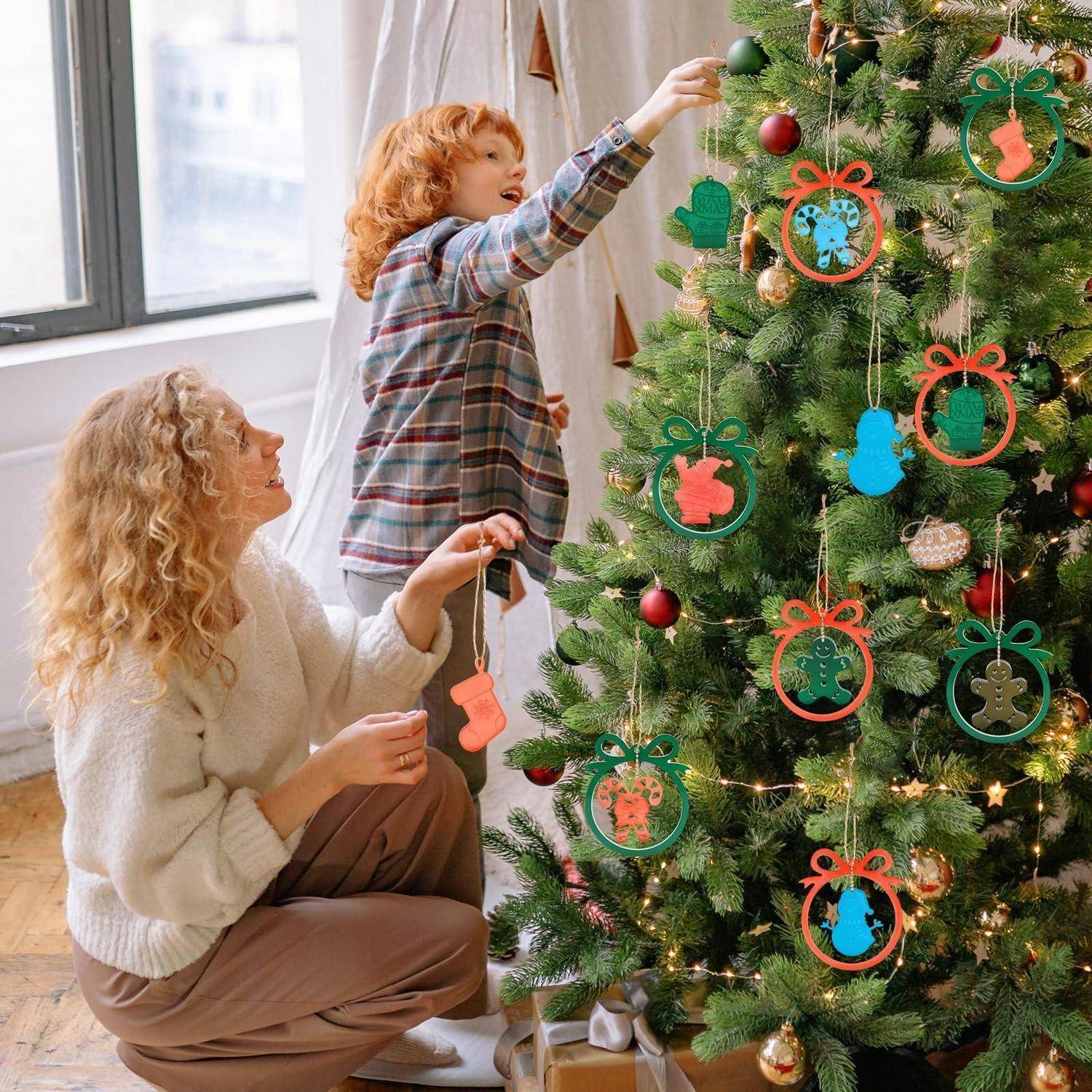 Kind und Frau schmücken einen Weihnachtsbaum mit farbigen Schmuckrahmen in einem hellen Wohnzimmer.