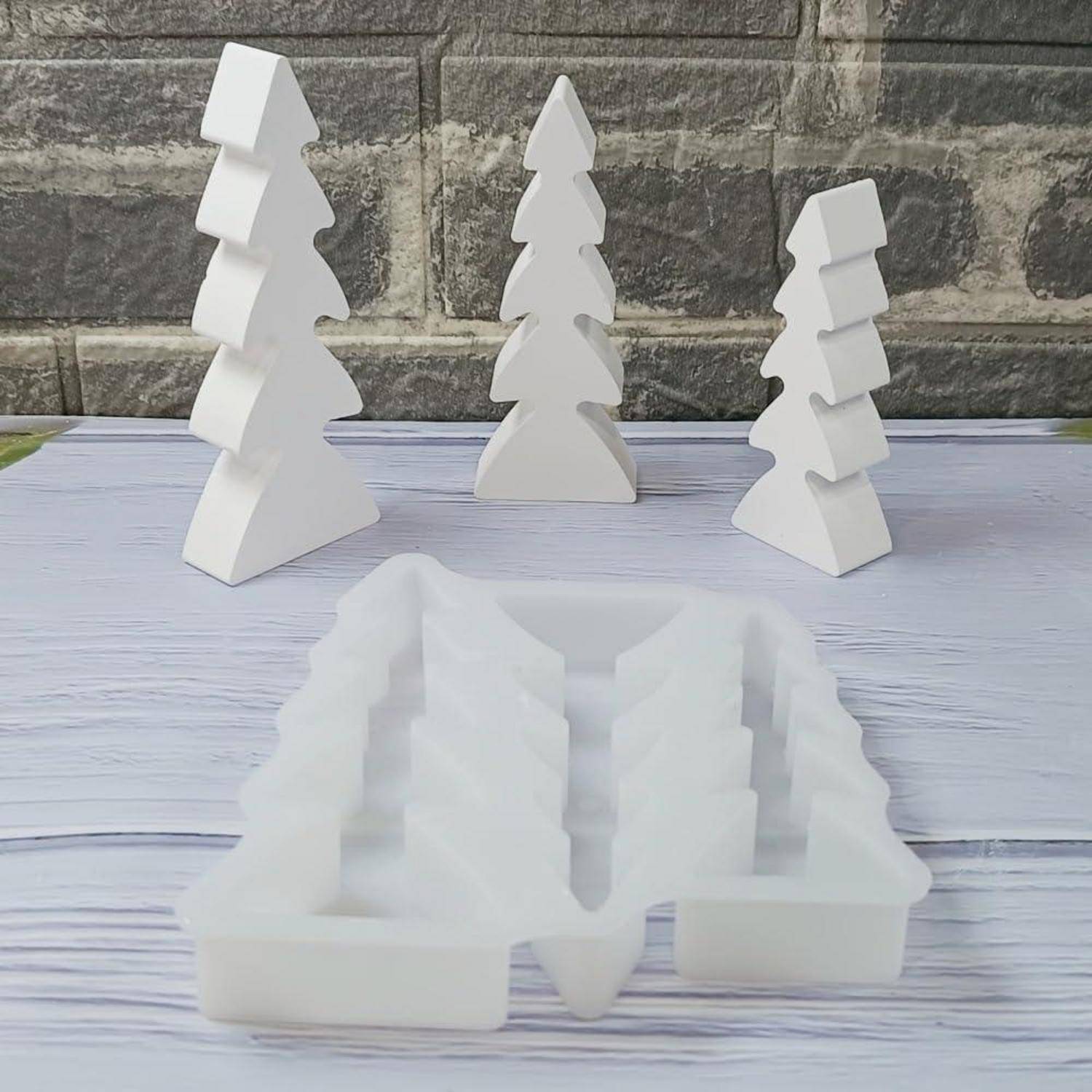 Weiße 3D-geometrische Kiefernbaumdekorationen stehen auf einer Tischplatte, mit einem gefrosteten weißen baumförmigen Halter im Vordergrund.