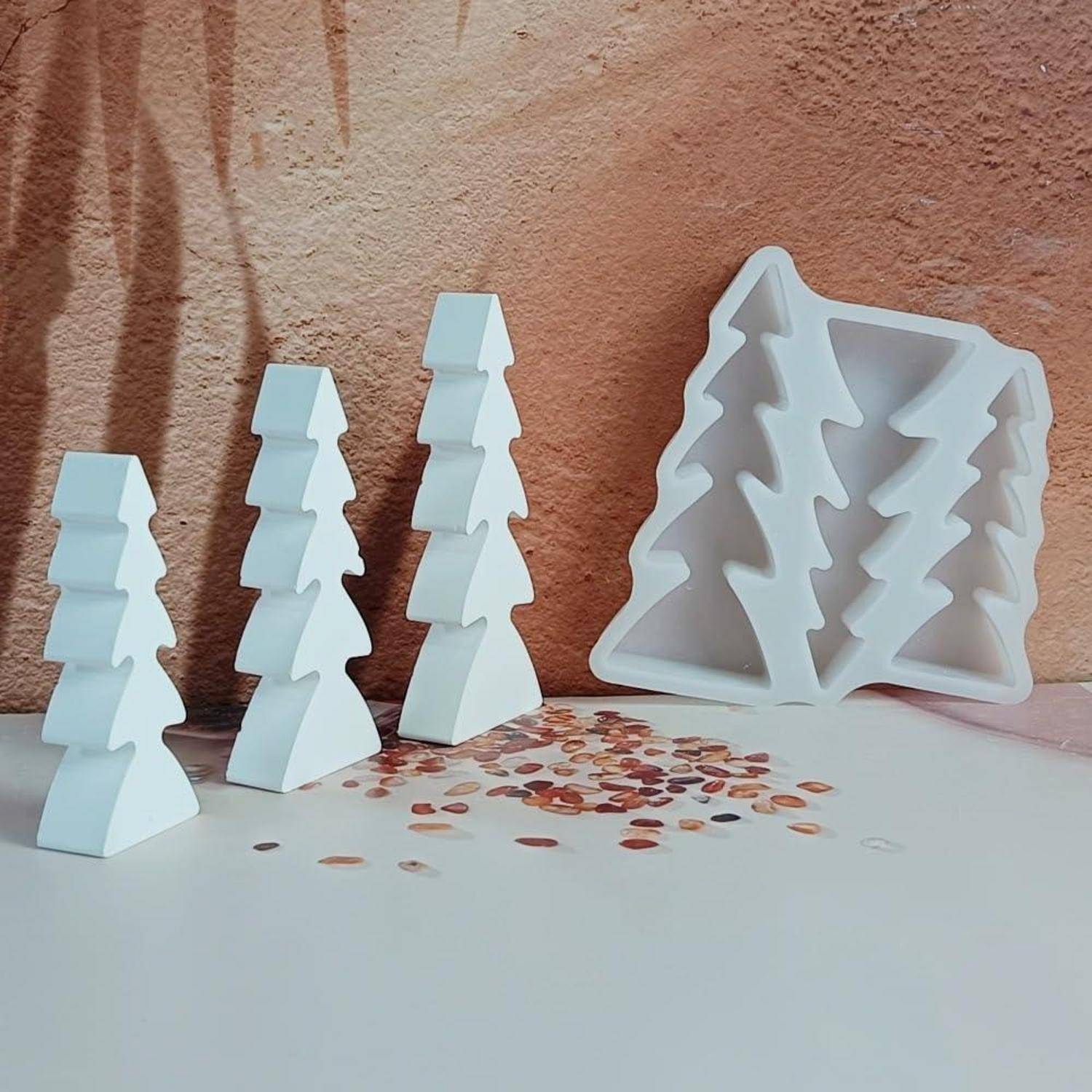 Weiße geometrische baumförmige Behälter oder Dekorationsstücke, die auf einer weißen Oberfläche neben einem größeren offenen Tablett angeordnet sind, vor einer strukturierten pfirsichfarbenen Wand.