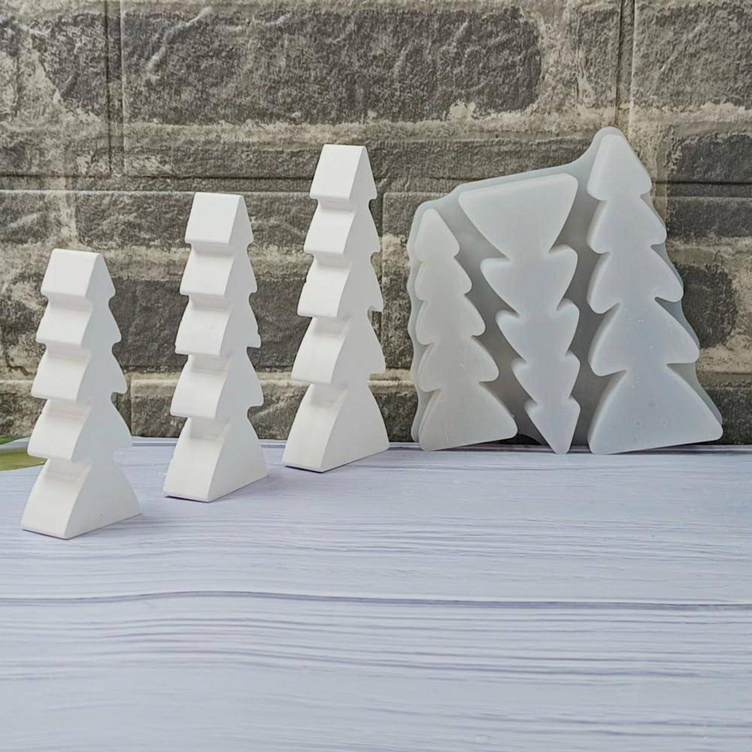 Weiße geometrische baumförmige Ornamente oder Skulpturen, die auf einer hellen Tischplatte angeordnet sind, vor einem Natursteinwand-Hintergrund.