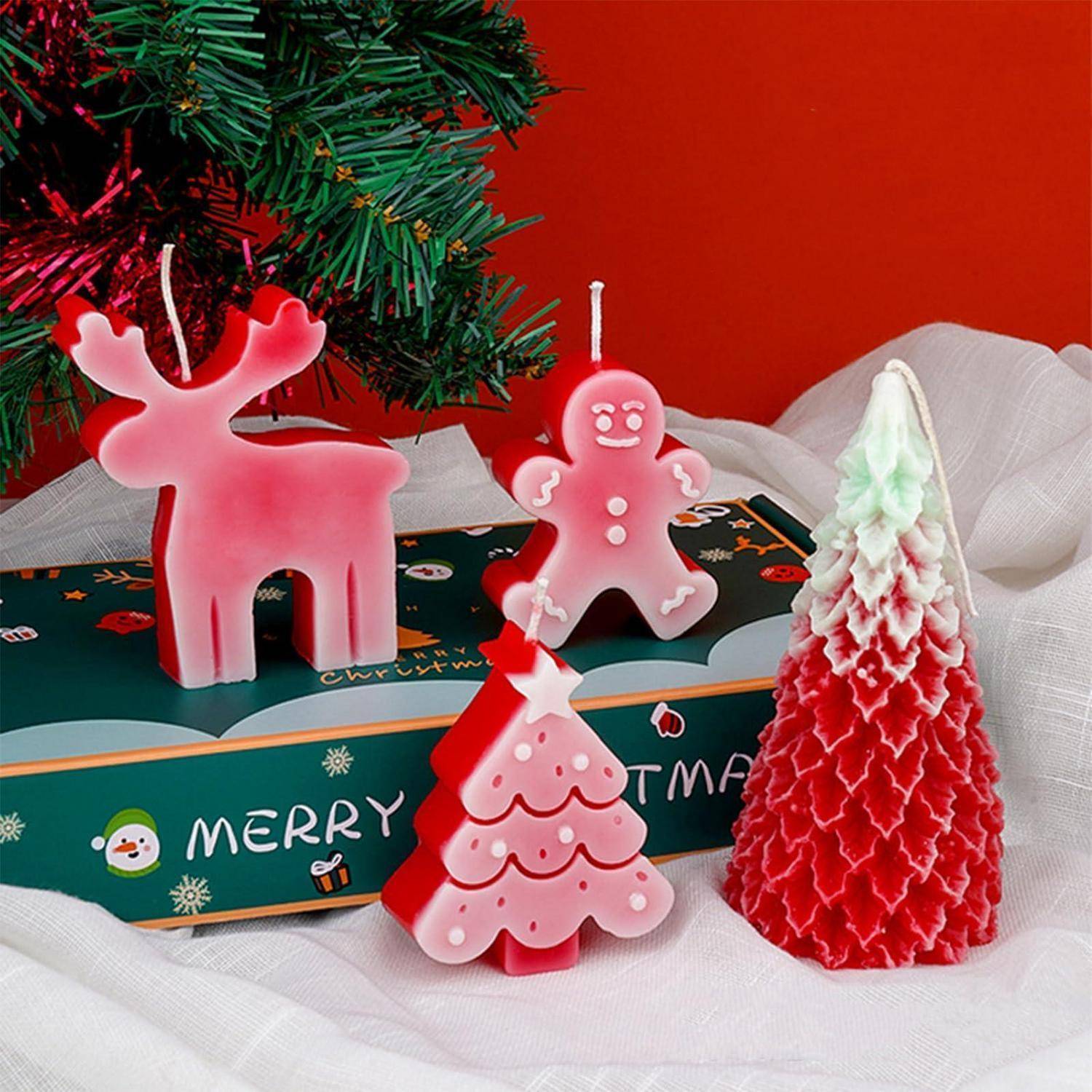 Weihnachtsthematische Kerzen in Form eines Rentiers, eines Lebkuchenmanns und von Bäumen, angeordnet mit einer dekorierten Schachteln, auf der „MERRY" steht, unter einem Baumzweig.