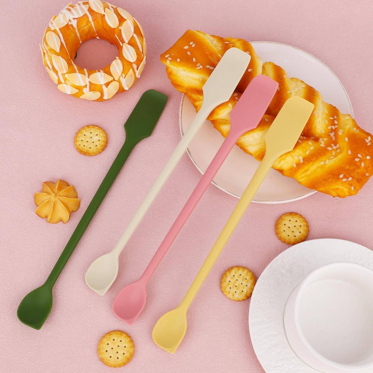 Pastellfarbene Küchenutensilien, die um ein glasiertes Gebäck angeordnet sind, mit einem Donut, Keksen und leeren Tellern auf einem rosa Hintergrund.
