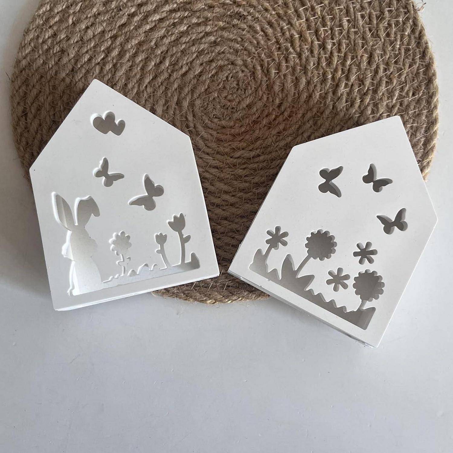 Zwei weiße, hausförmige Ausschnittskarten mit Schmetterlings- und Blumensilhouetten, die gegen eine geflochtene runde Matte angezeigt werden.