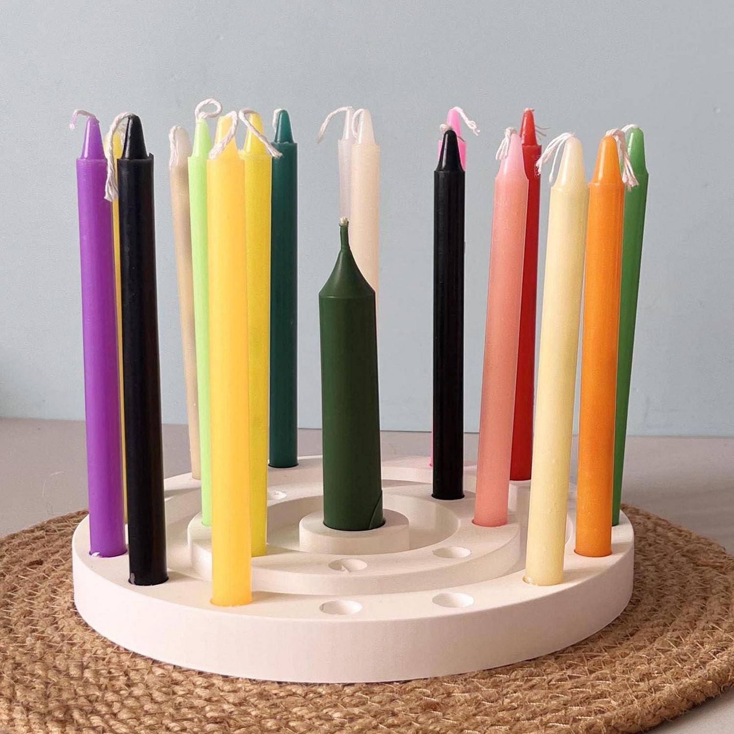 Bunte Kerzen in konischer Form in einem runden weißen Halter auf einer Flechtmatte, in einer spiralförmigen Anordnung angeordnet.