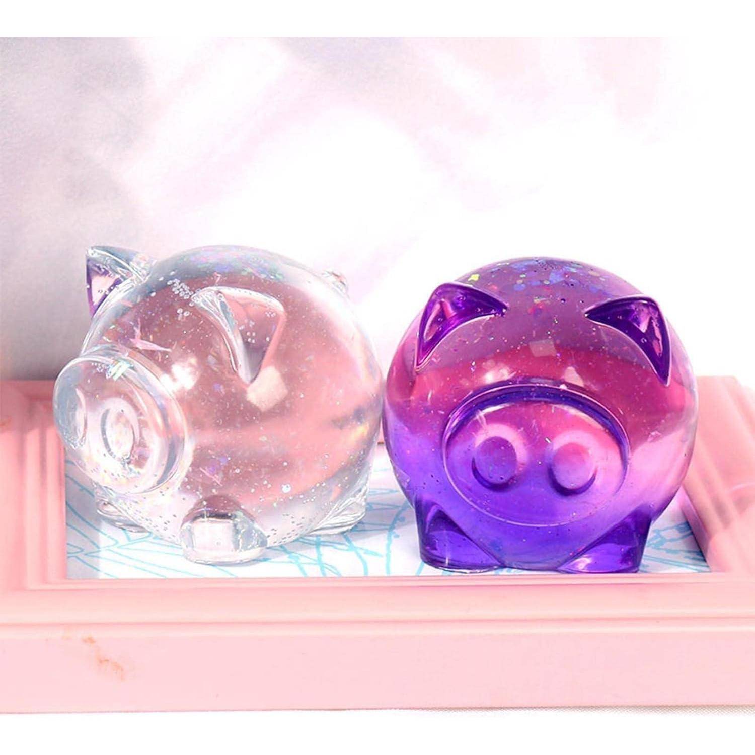 Zwei durchscheinbare Sparschweine, eines klar und eines lila, sitzen in einer rosa Schale vor einem sanften pastellfarbenen Hintergrund.